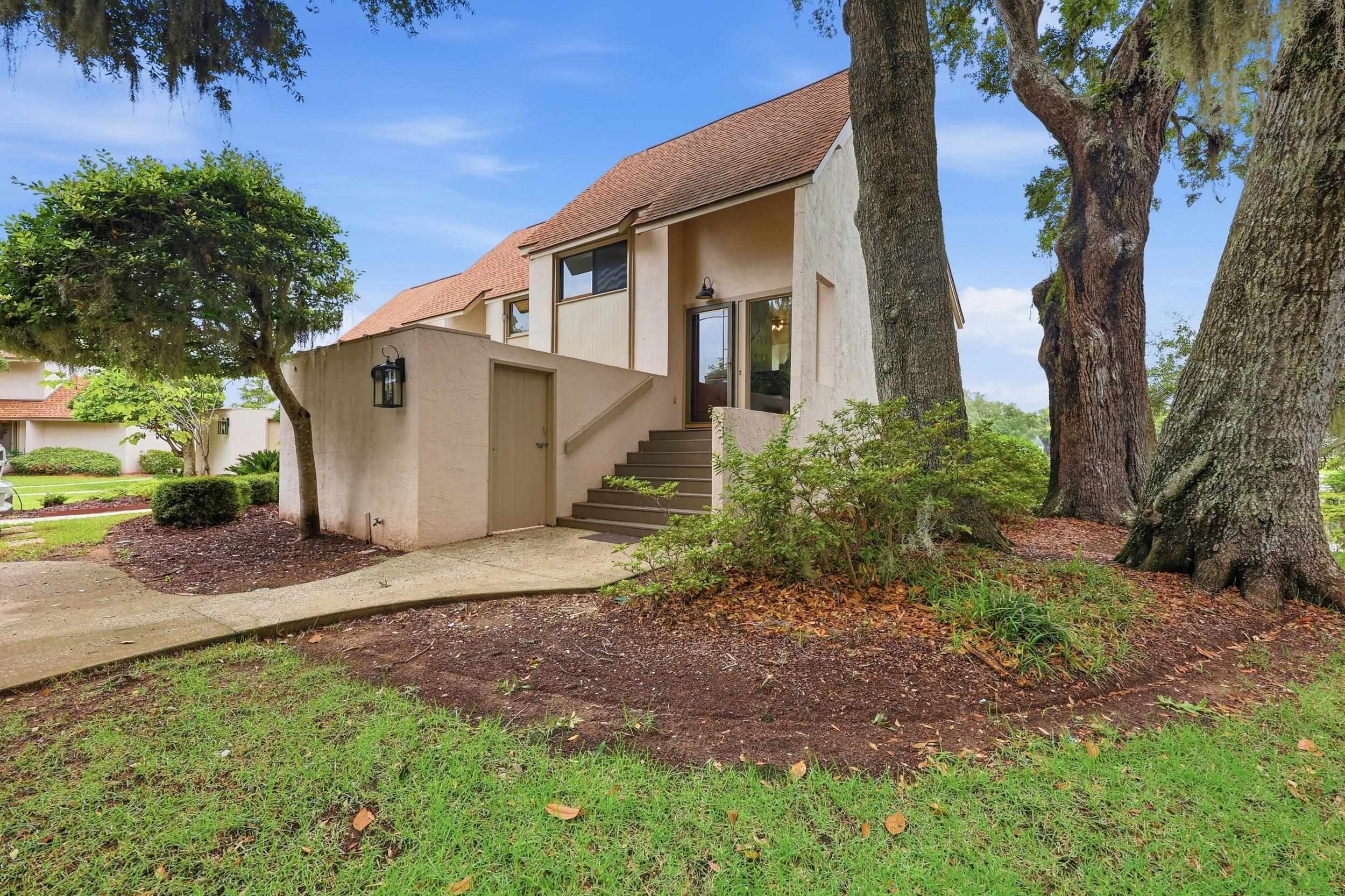 Beige two-story home with front steps framed by mature oak trees.