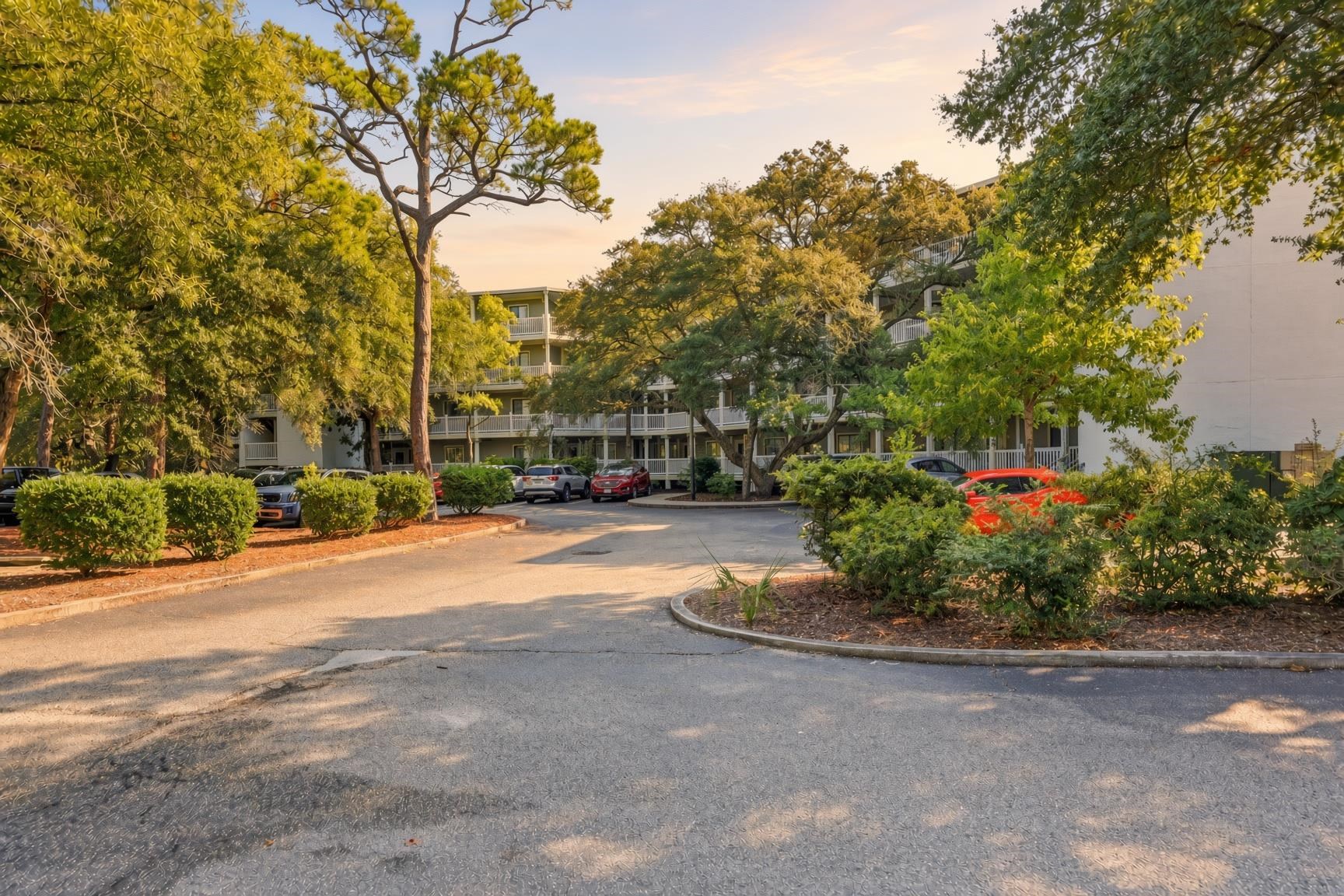 Multi-story condominium with balconies framed by mature trees and landscaped grounds.