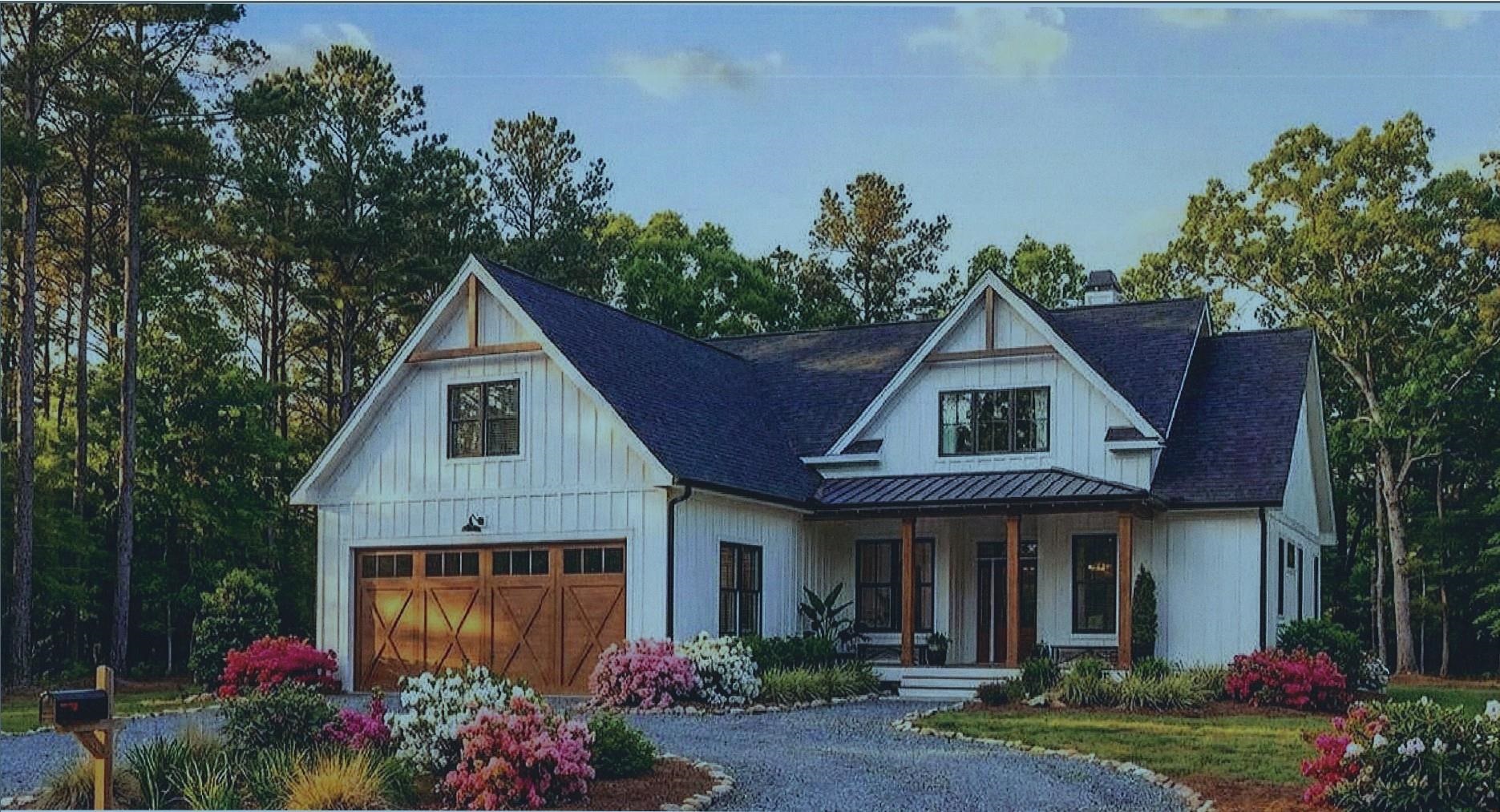 White farmhouse with a wooden garage door, covered porch, and colorful flowering landscaping.