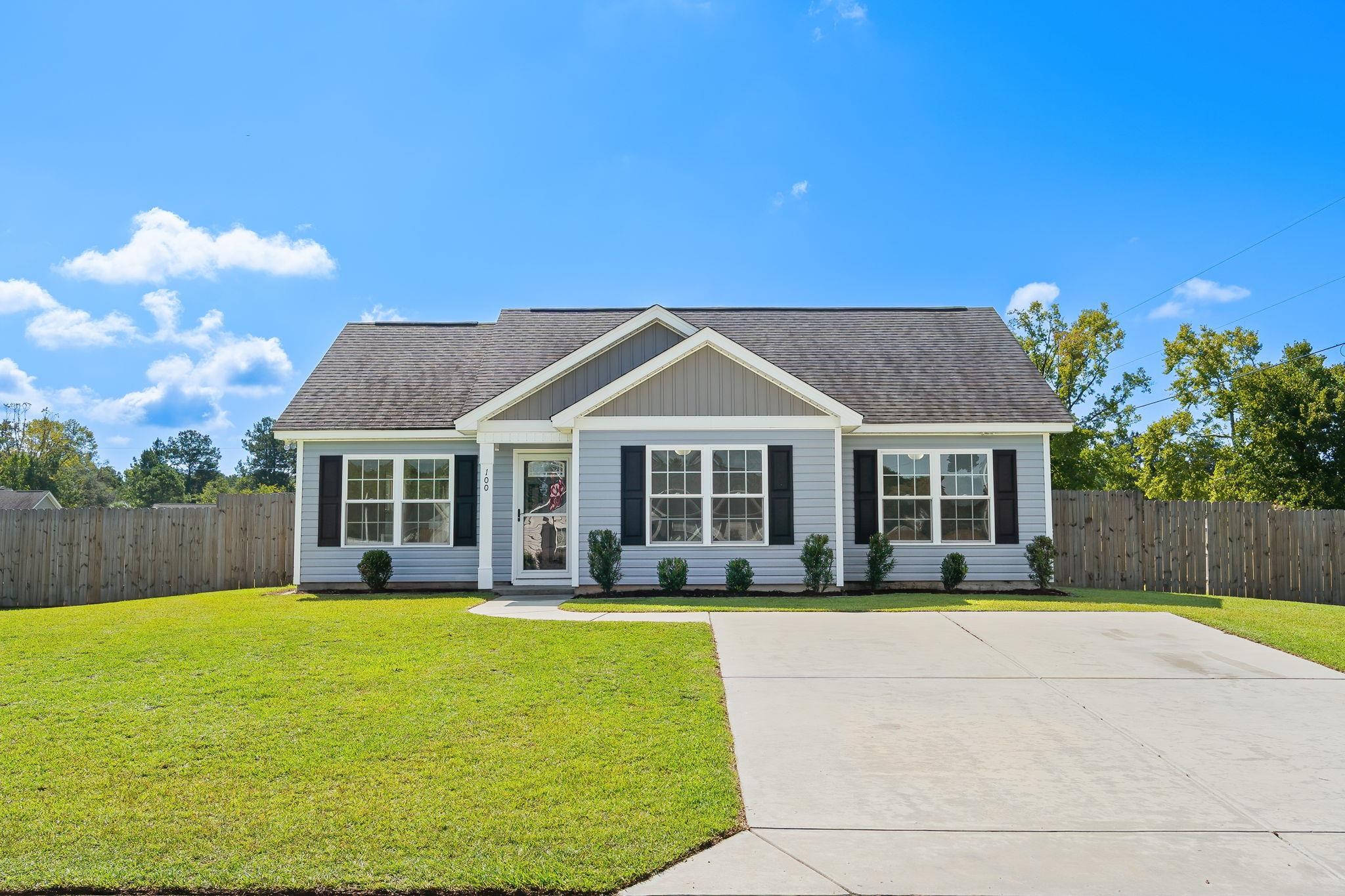 Single-story blue-gray home with a gabled roof, black shutters, broad driveway, and fenced lawn.