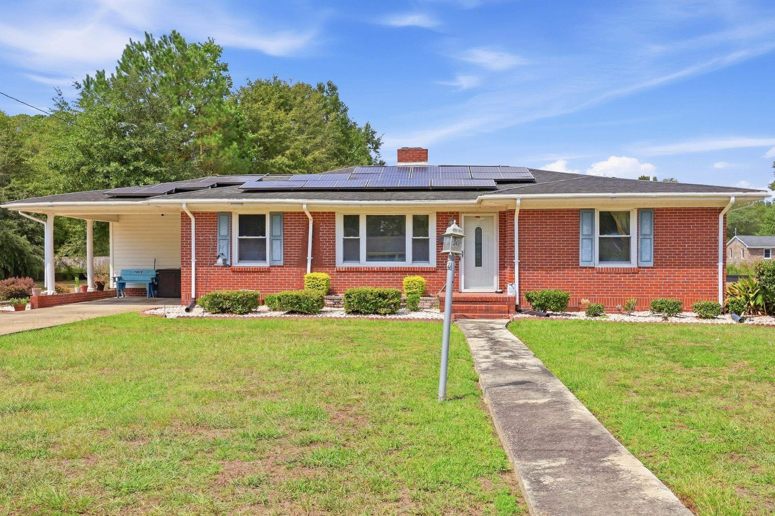 Single-story brick house with rooftop solar panels, a covered carport, and a walkway across the lawn.
