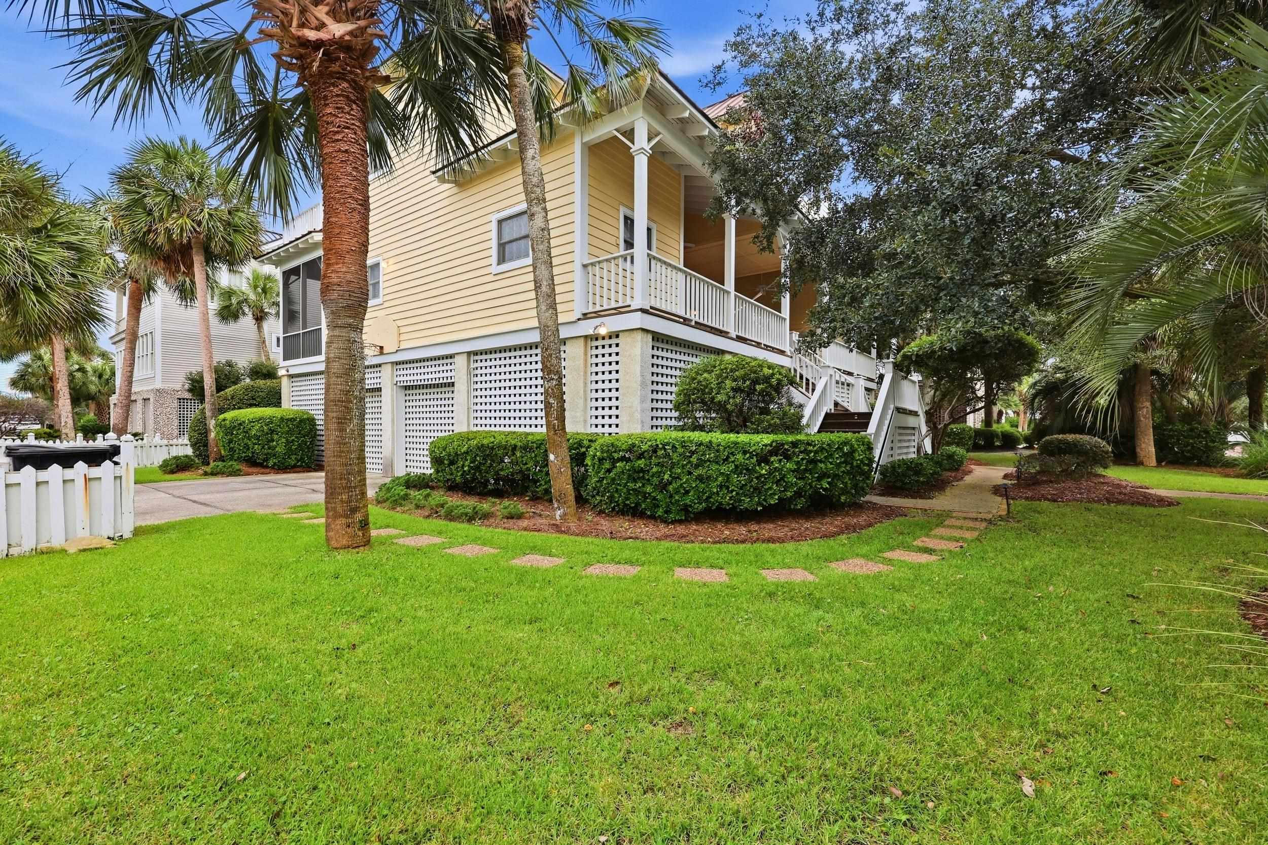 Pale yellow raised home with a covered porch, white lattice foundation, and palm trees around a green lawn.