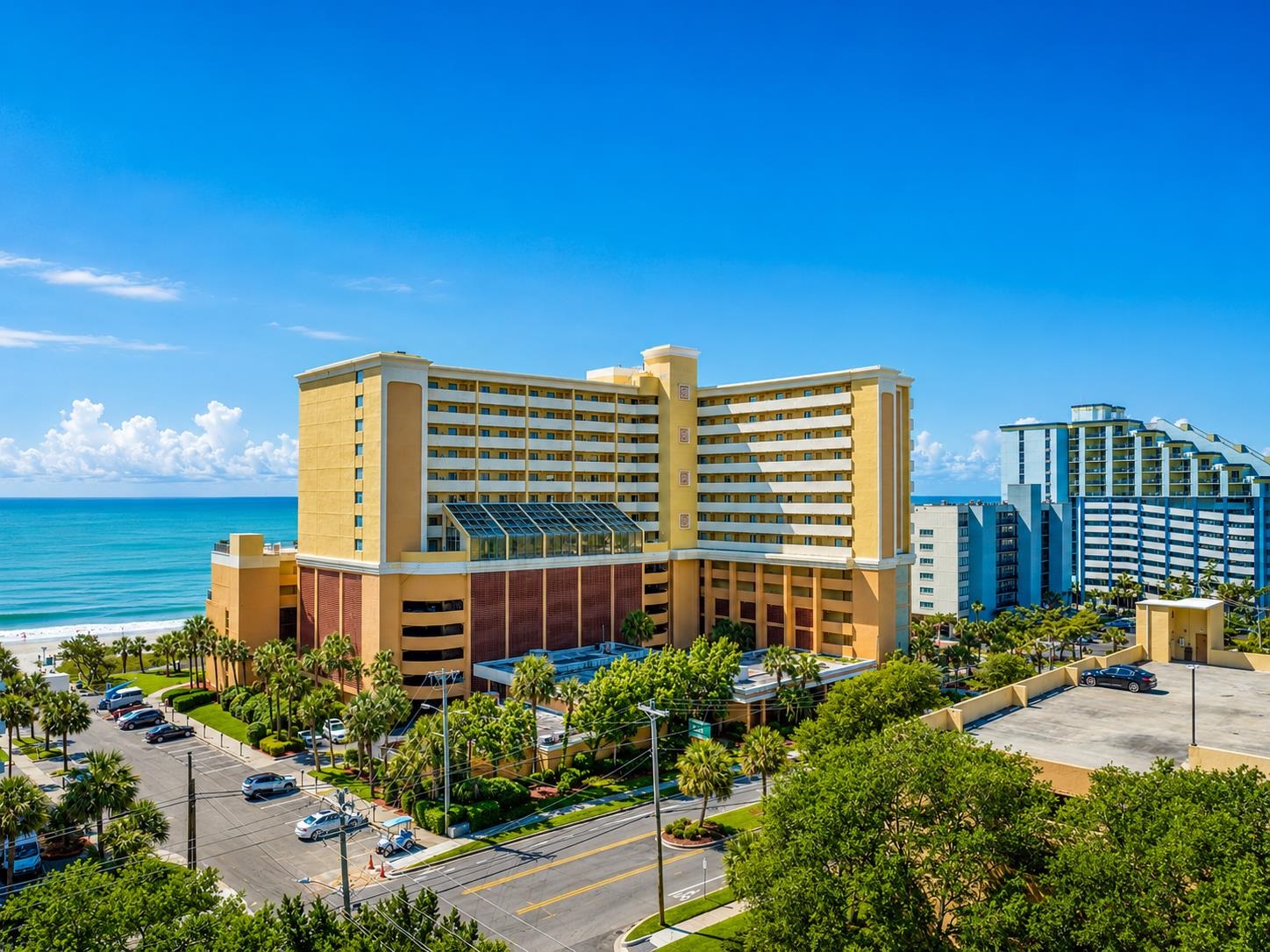 Oceanfront condominium tower with a yellow facade, landscaped grounds, and neighboring high-rises.