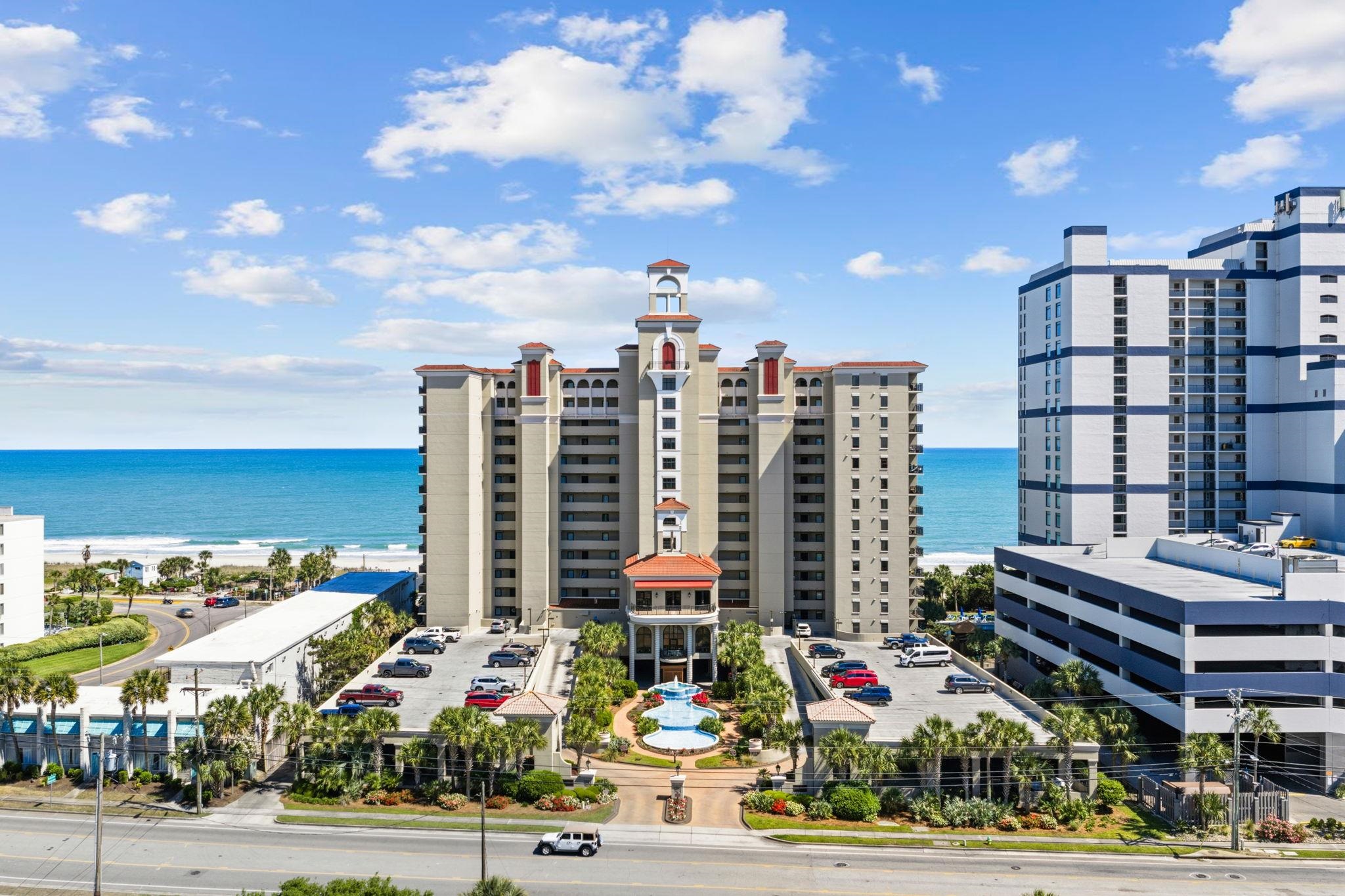 Beachfront condominium tower with an entrance pool, landscaped grounds, and ocean behind it.