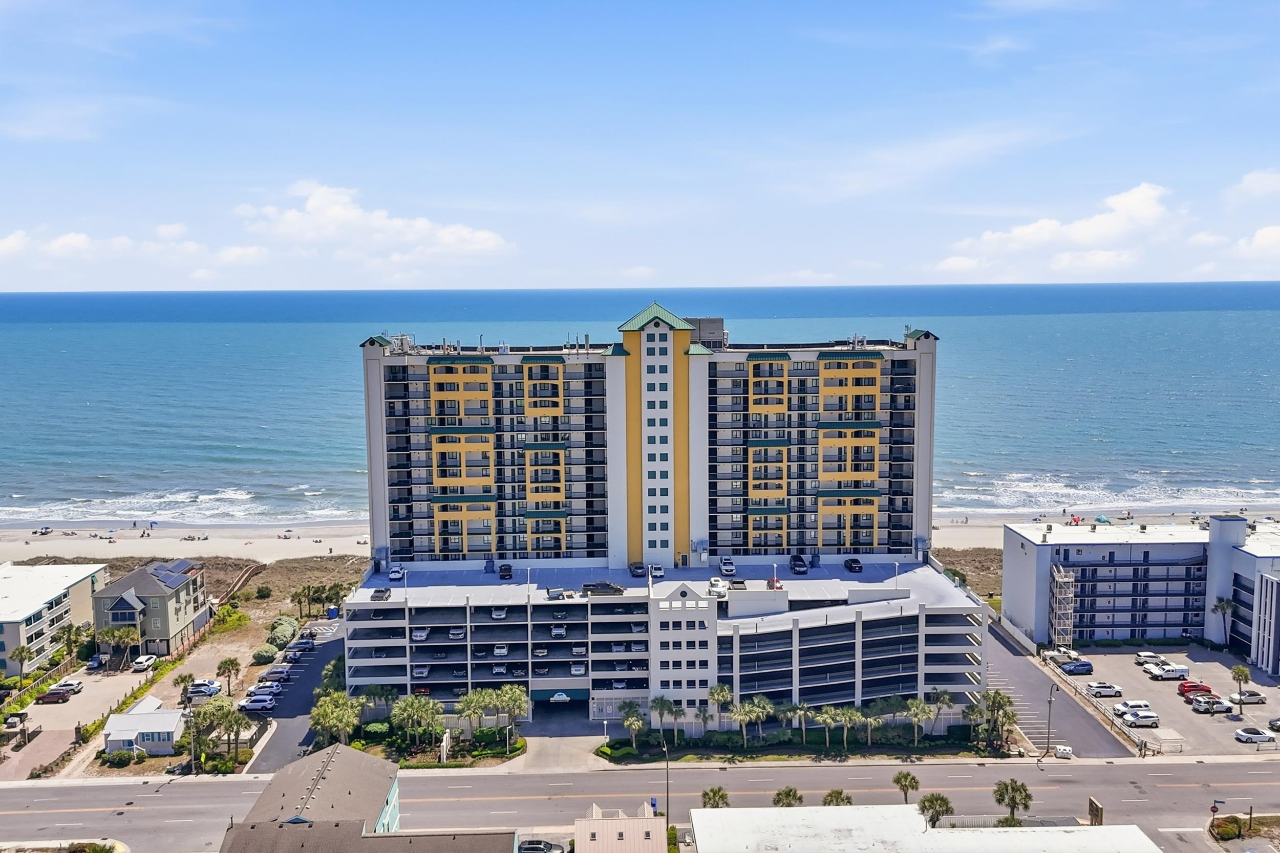 Beachfront condominium with a multilevel parking garage, sandy shore, and ocean behind it.