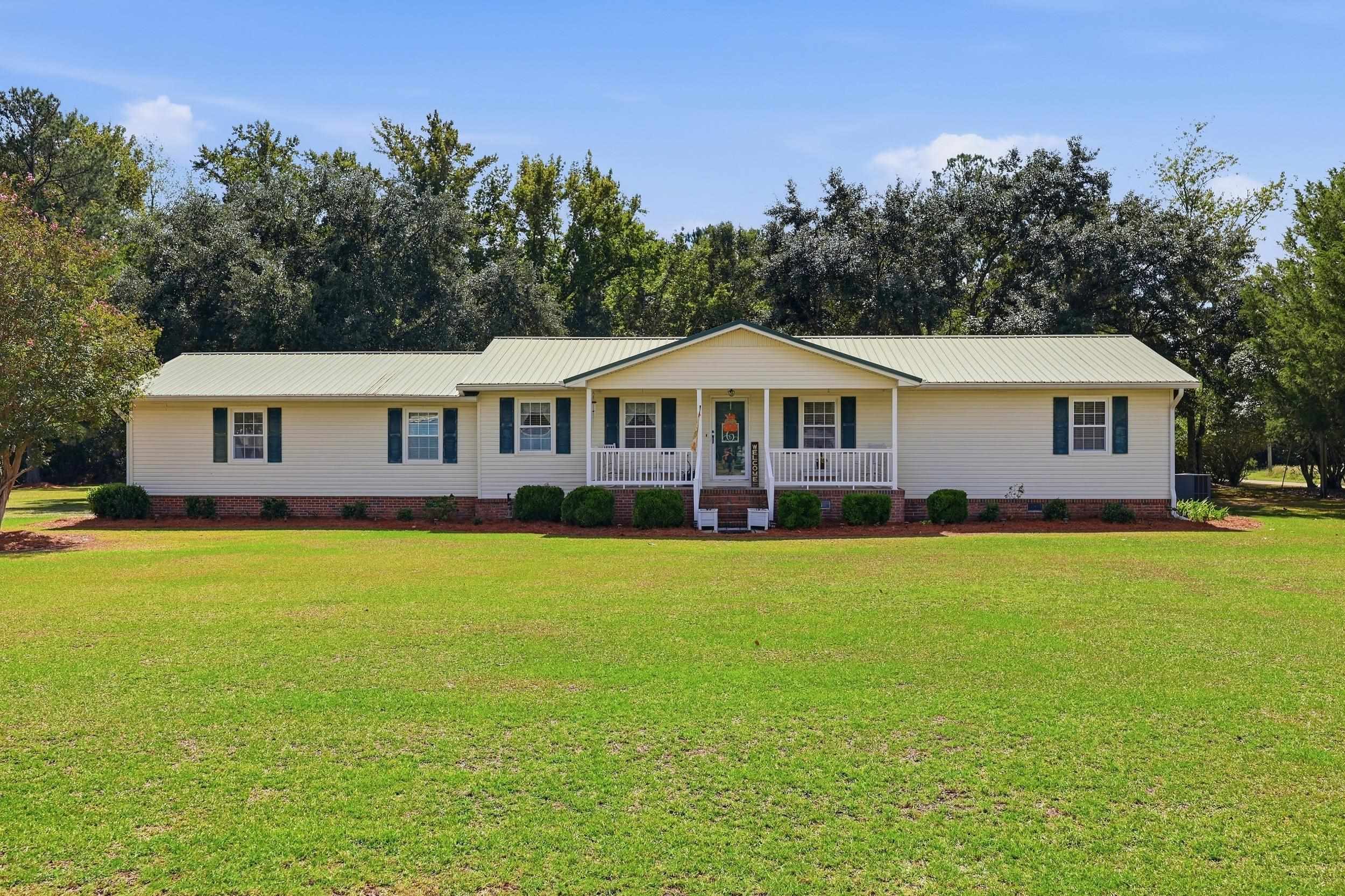 Single-story ranch home with a metal roof, covered porch, and broad green lawn.