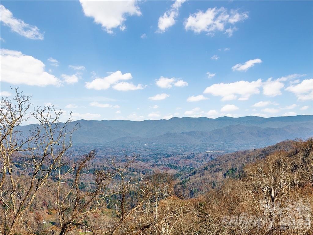 Mountain valley view beneath a broad blue sky, framed by leafless trees.