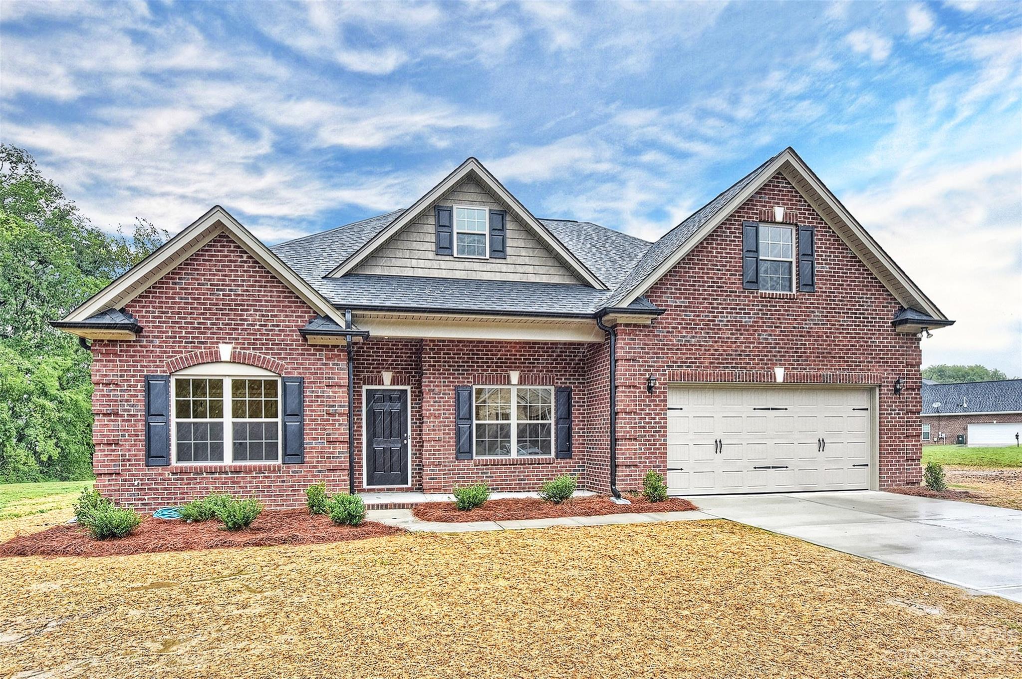 Red-brick house with several front gables, dark shutters, and an attached two-car garage.