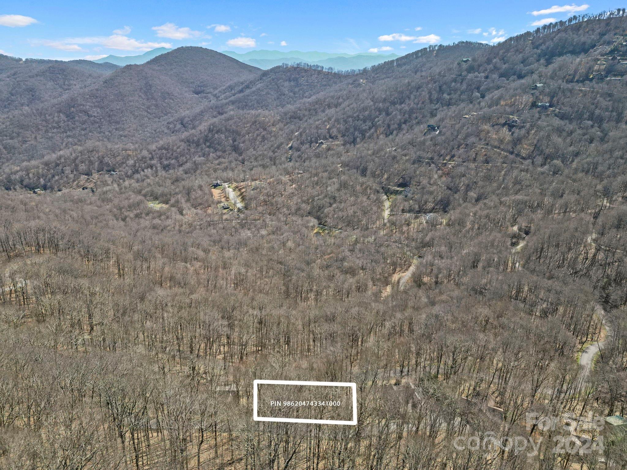 Aerial view of a wooded mountain property marked with a white parcel boundary.