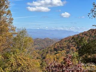 Wooded mountain ridges in autumn beneath a partly cloudy blue sky.