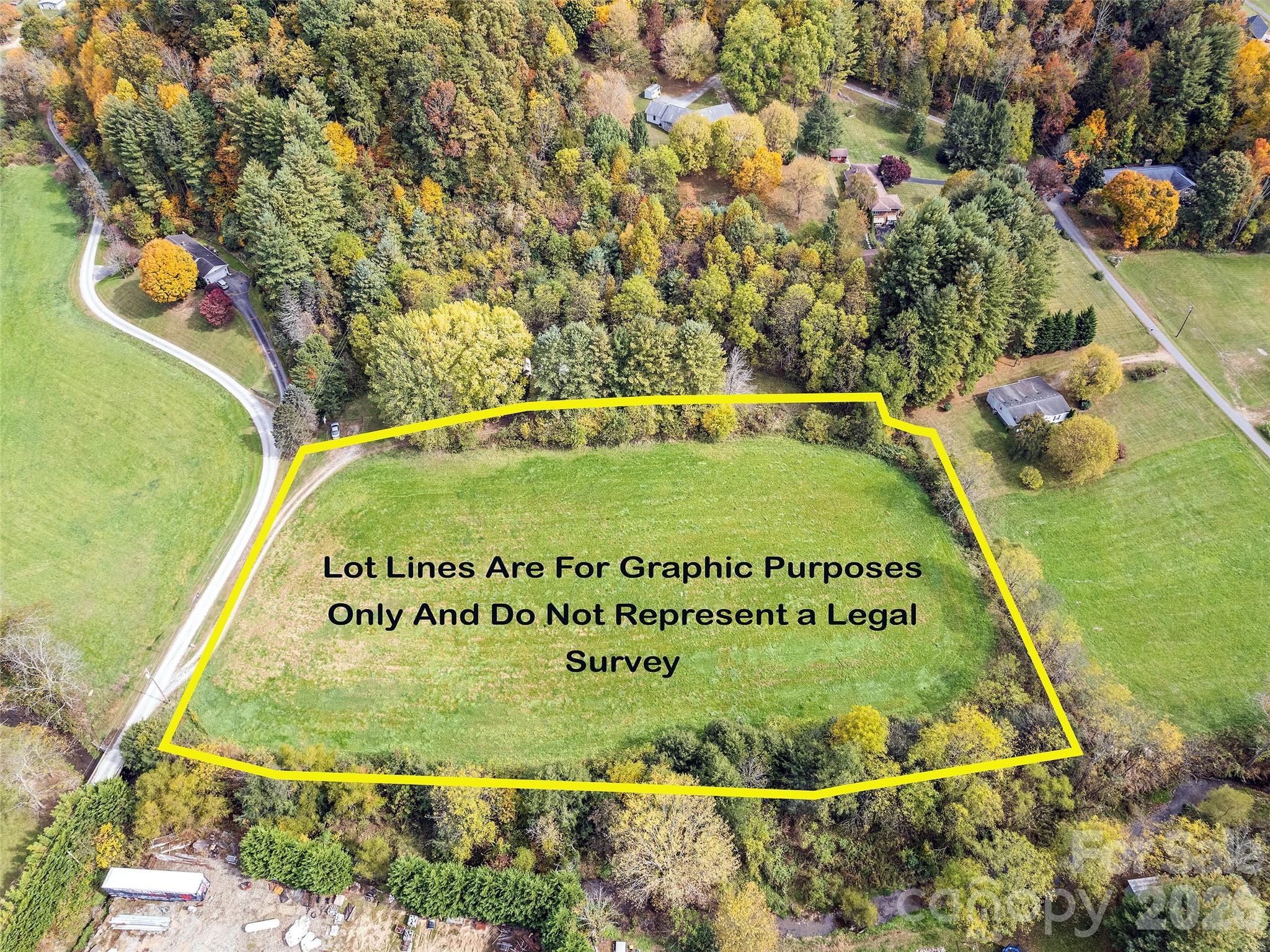 Aerial view of a grassy parcel outlined in yellow amid autumn woods and rural homes.