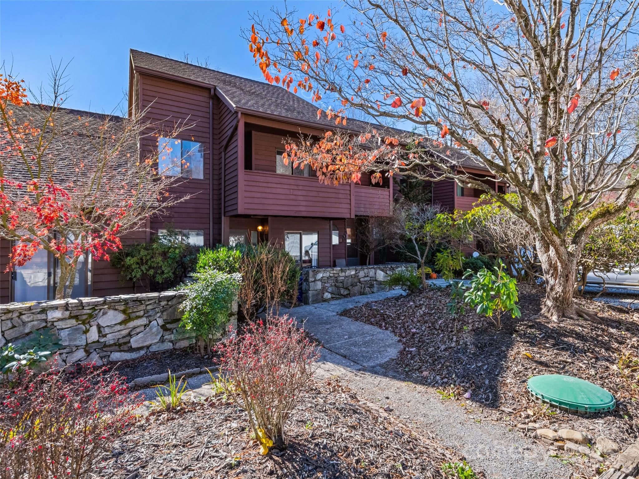 Wood-sided home with stone retaining walls and a landscaped front walkway beneath autumn trees.