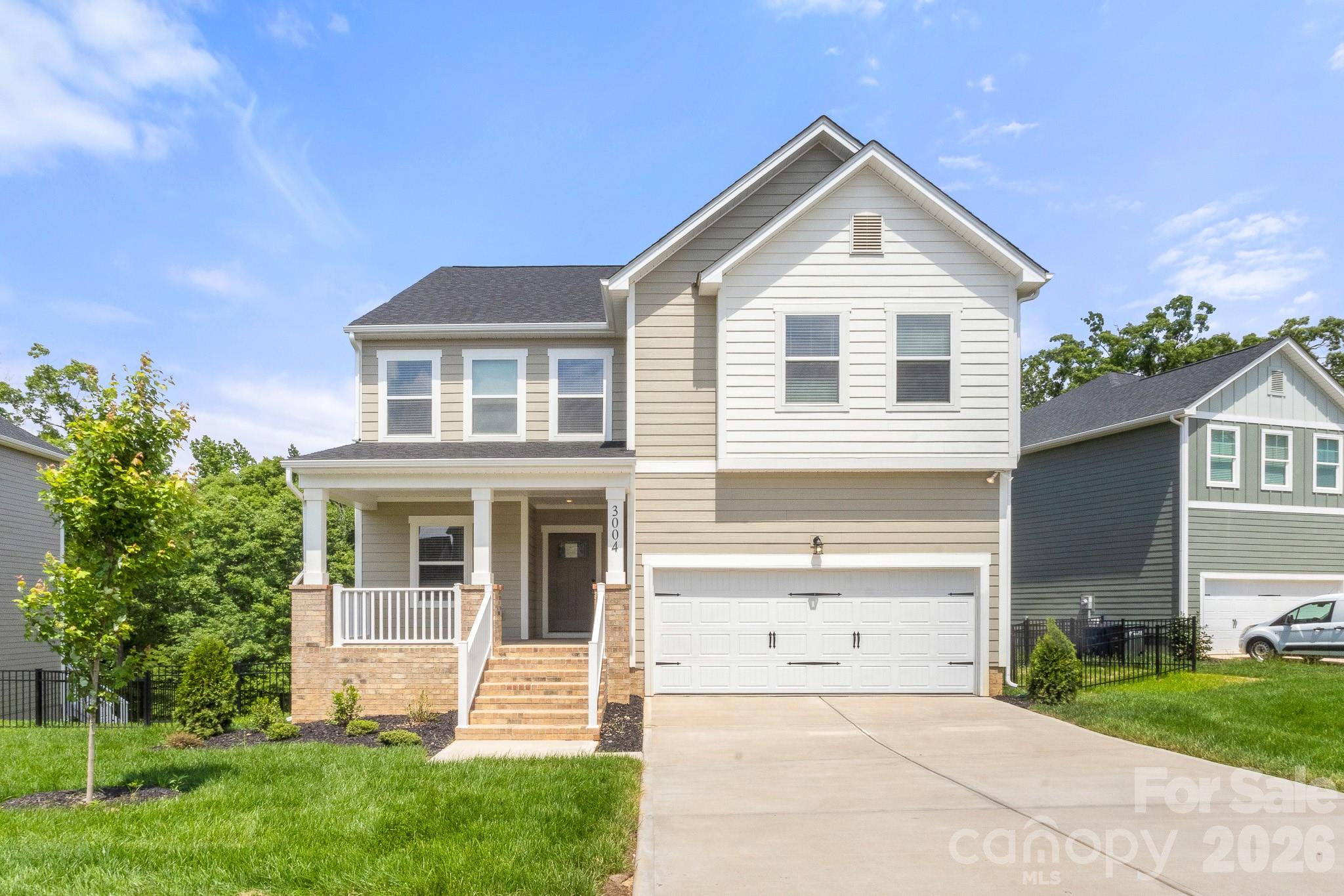 Two-story beige house with a covered porch, brick steps, and an attached double garage.