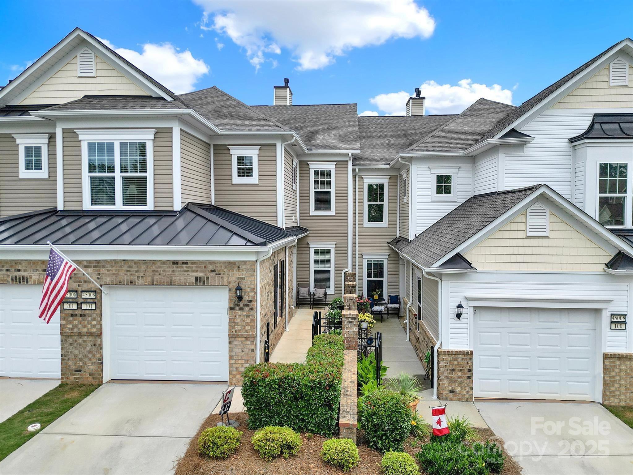 Attached townhomes with garages, a landscaped walkway, and American and Canadian flags.