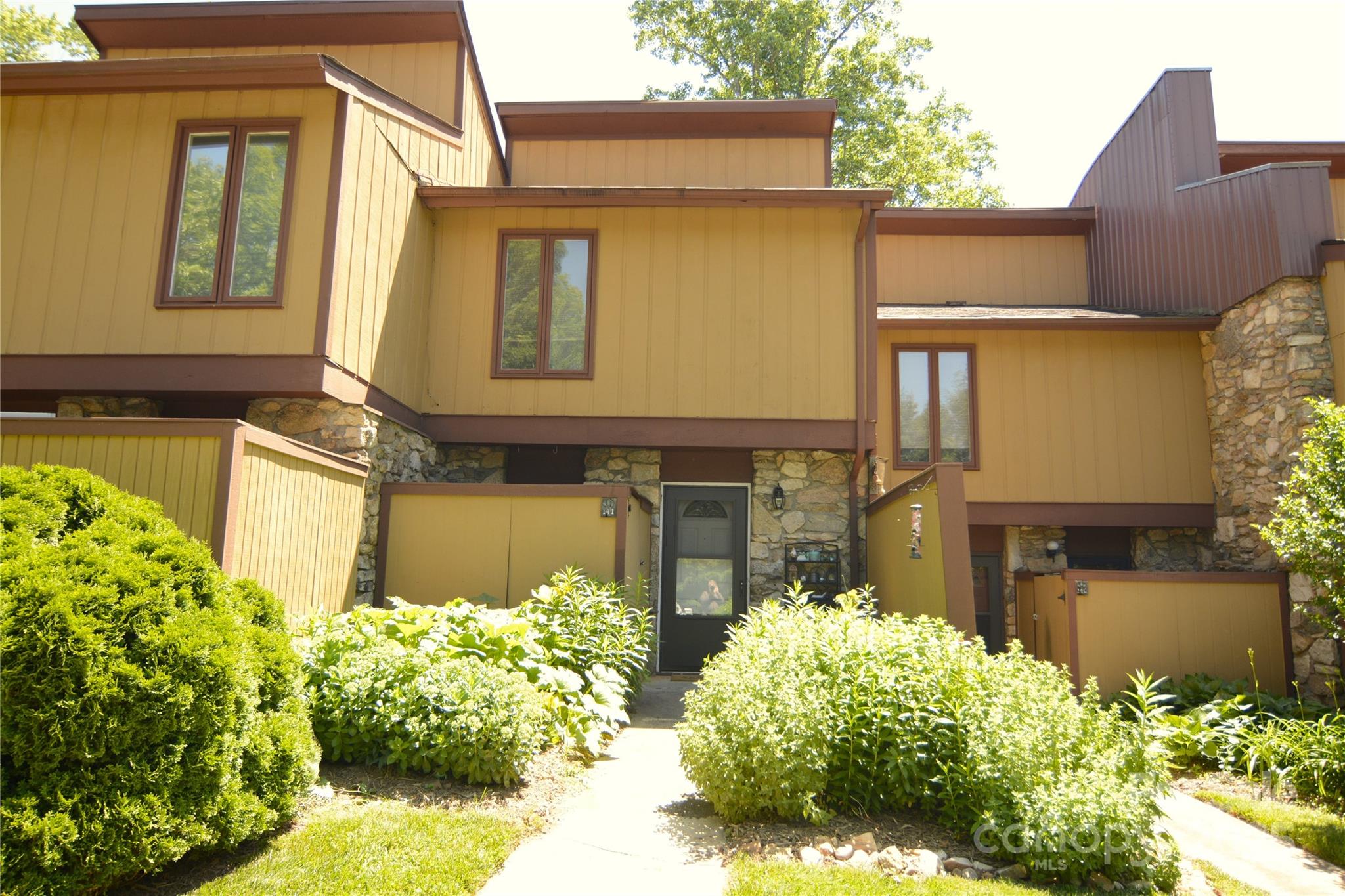 Multilevel yellow-sided home with stone accents and a landscaped walkway to the front entrance.
