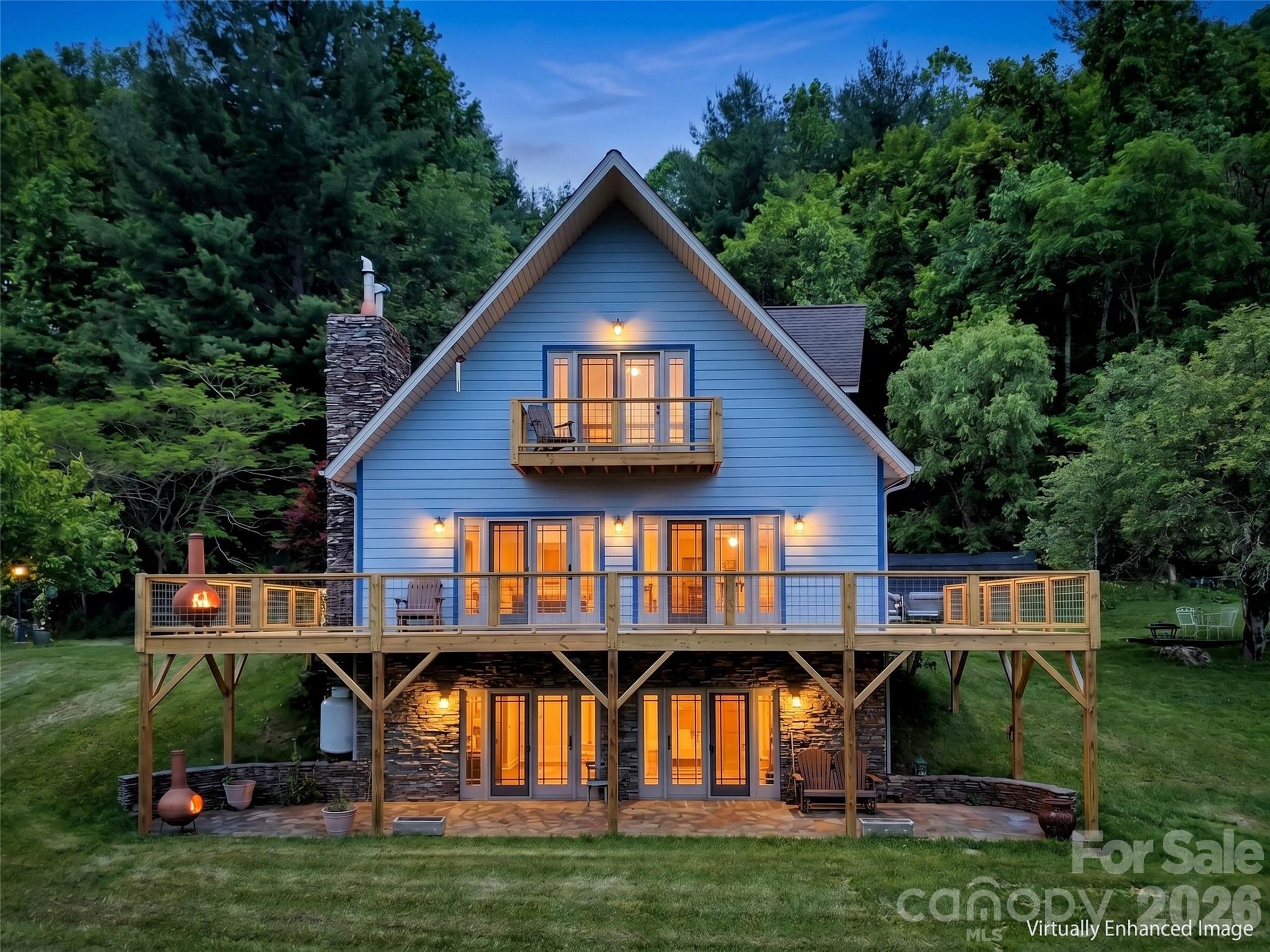 Blue A-frame home with expansive multi-level decks glowing with warm light at dusk among trees.