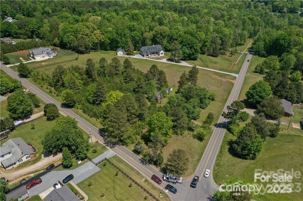 Aerial view of a house on a spacious wooded property bordered by two roads.
