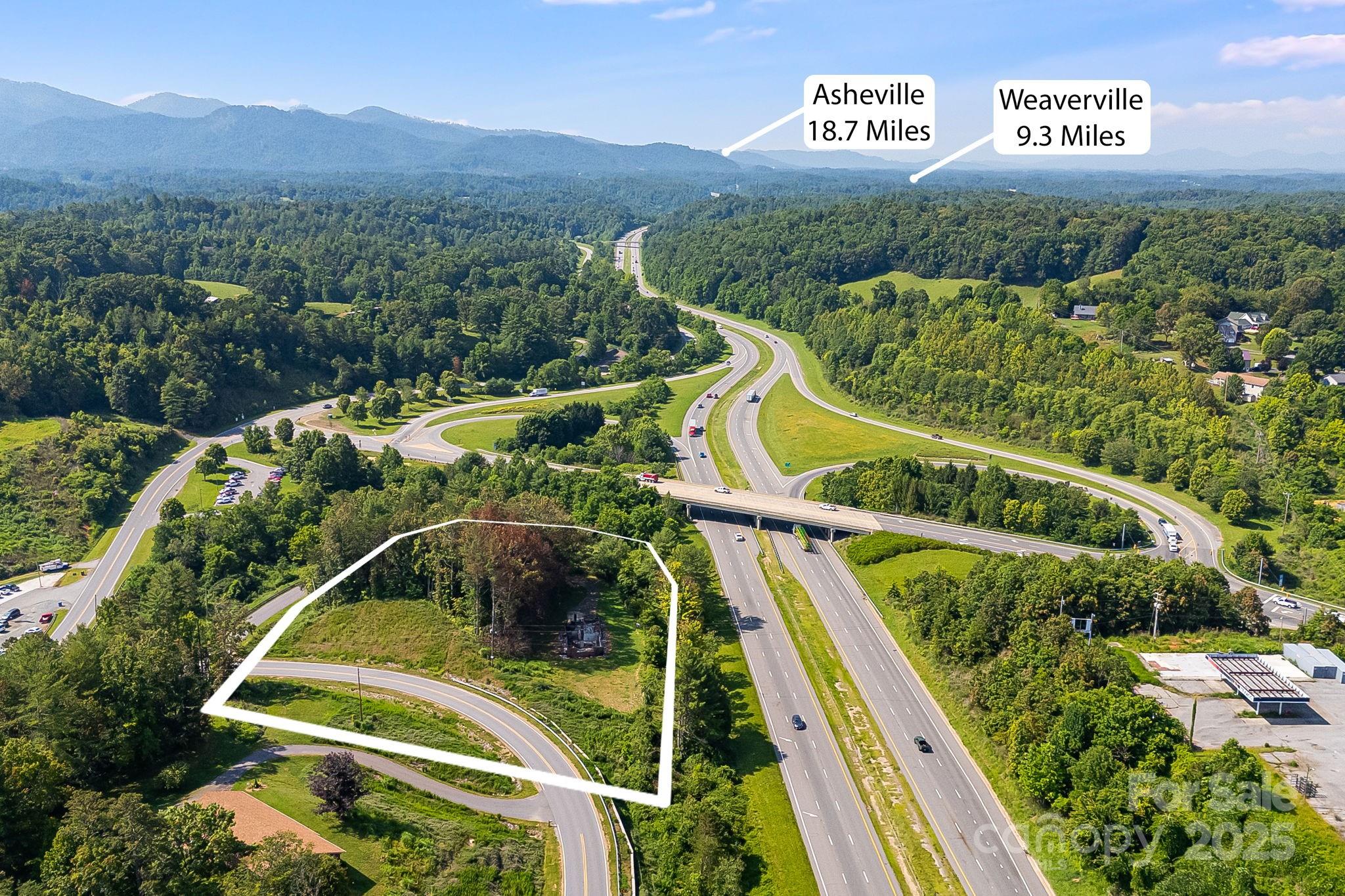 A wooded parcel outlined beside a highway interchange, with mountains in the distance.