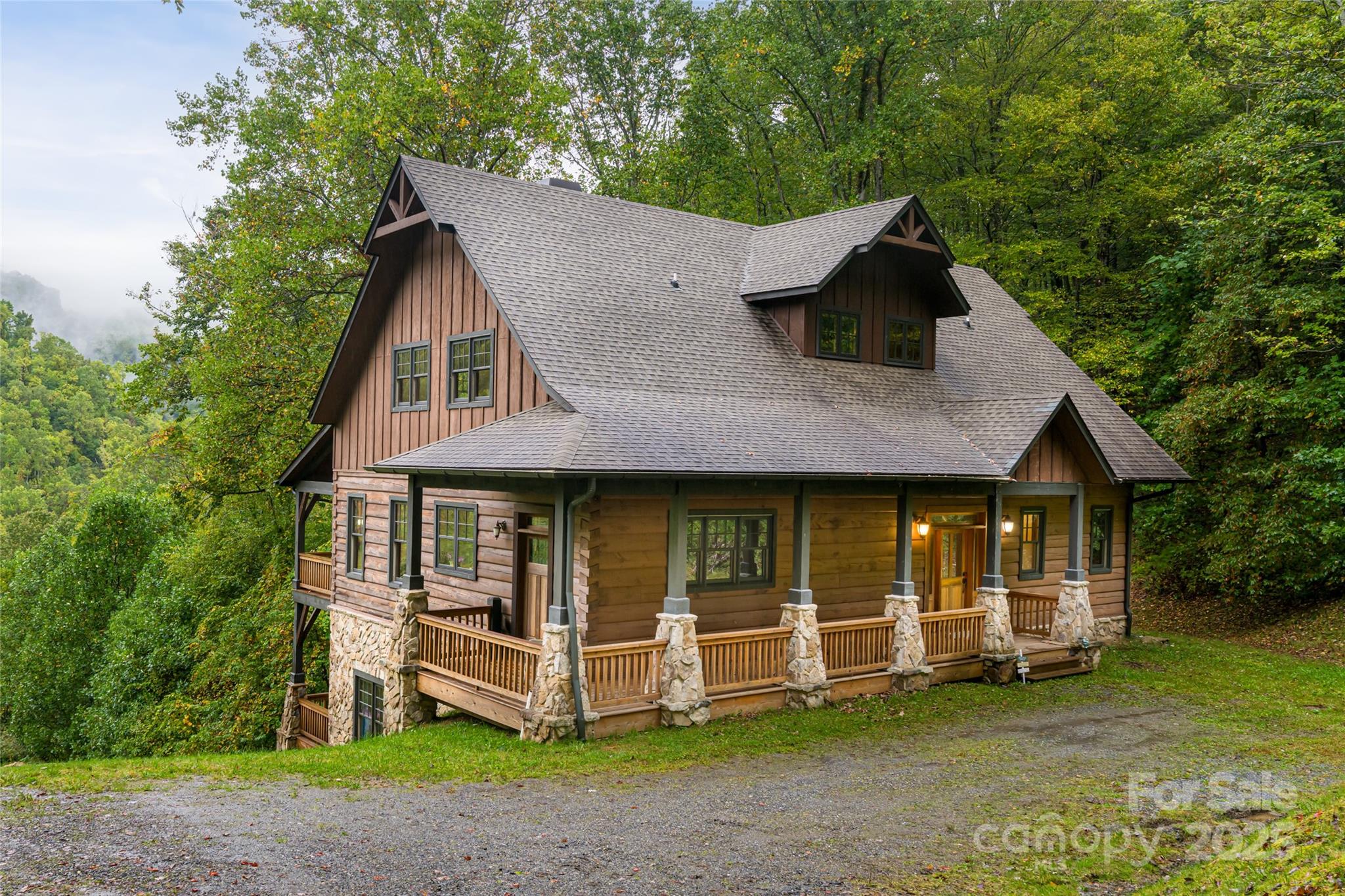 Wood-and-stone mountain home with a wraparound porch, surrounded by trees.