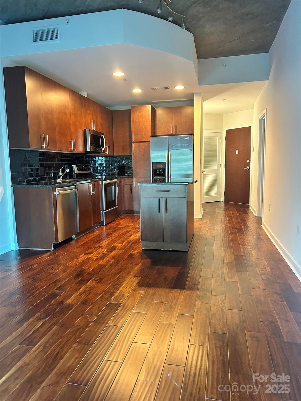 Apartment kitchen with wood cabinets, stainless steel appliances, a central island, and glossy wood-look flooring.