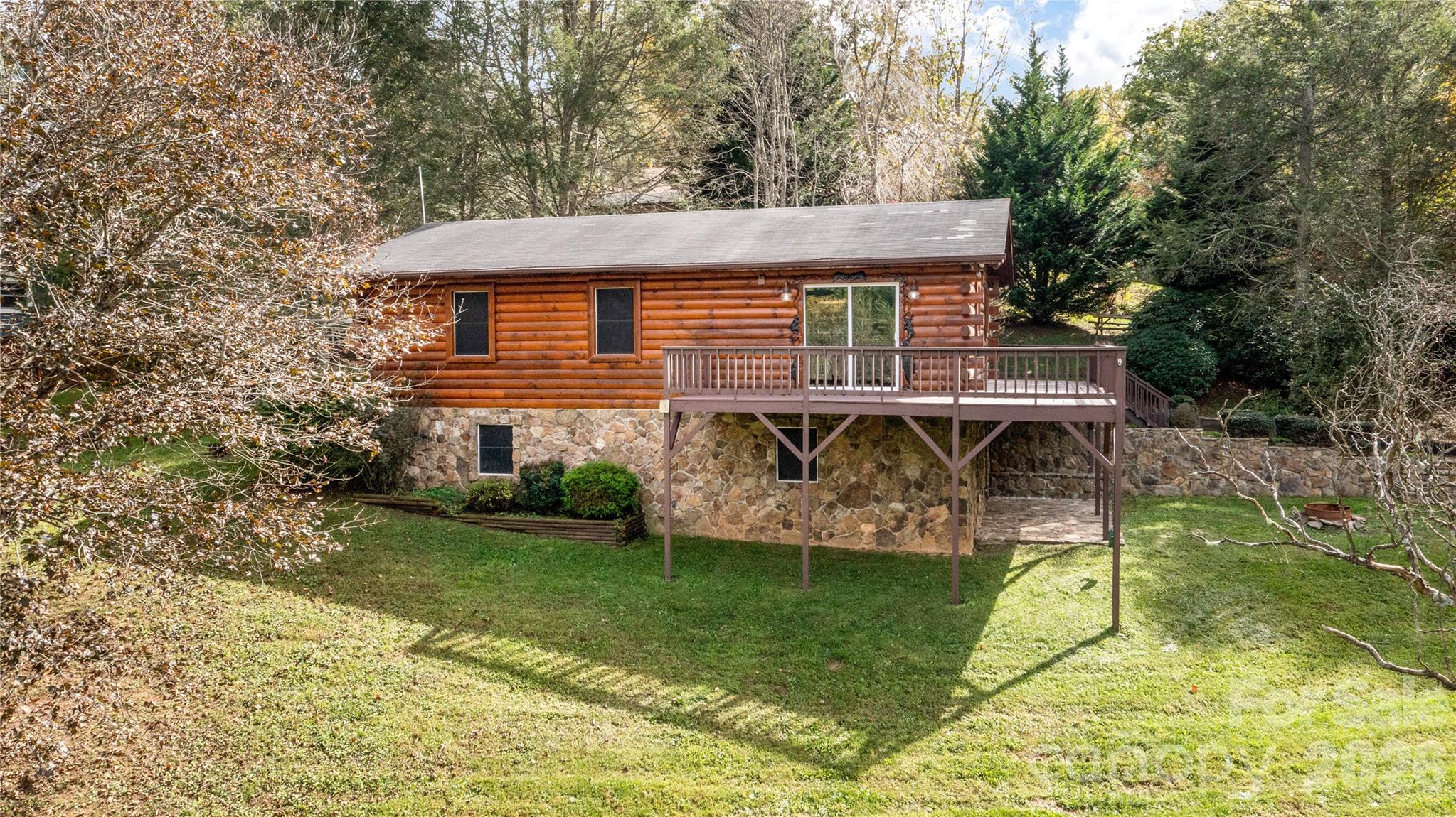 Log cabin with a raised deck and stone foundation in a wooded yard.