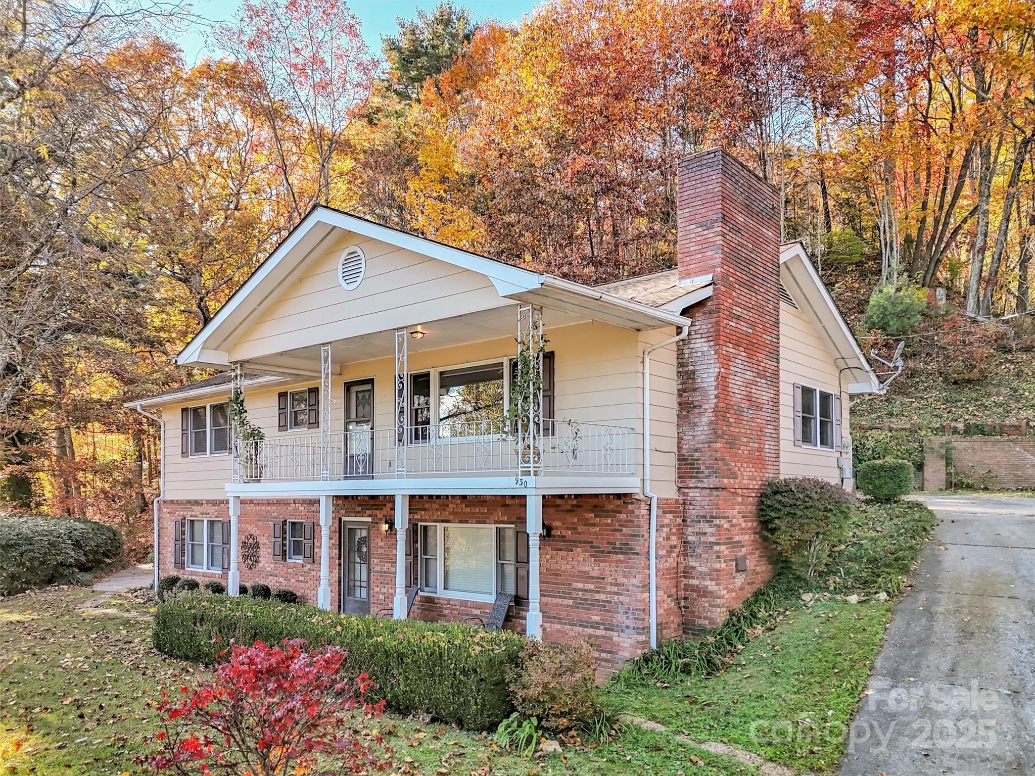 Two-story cream-sided and brick home with a covered porch and tall chimney amid autumn foliage.