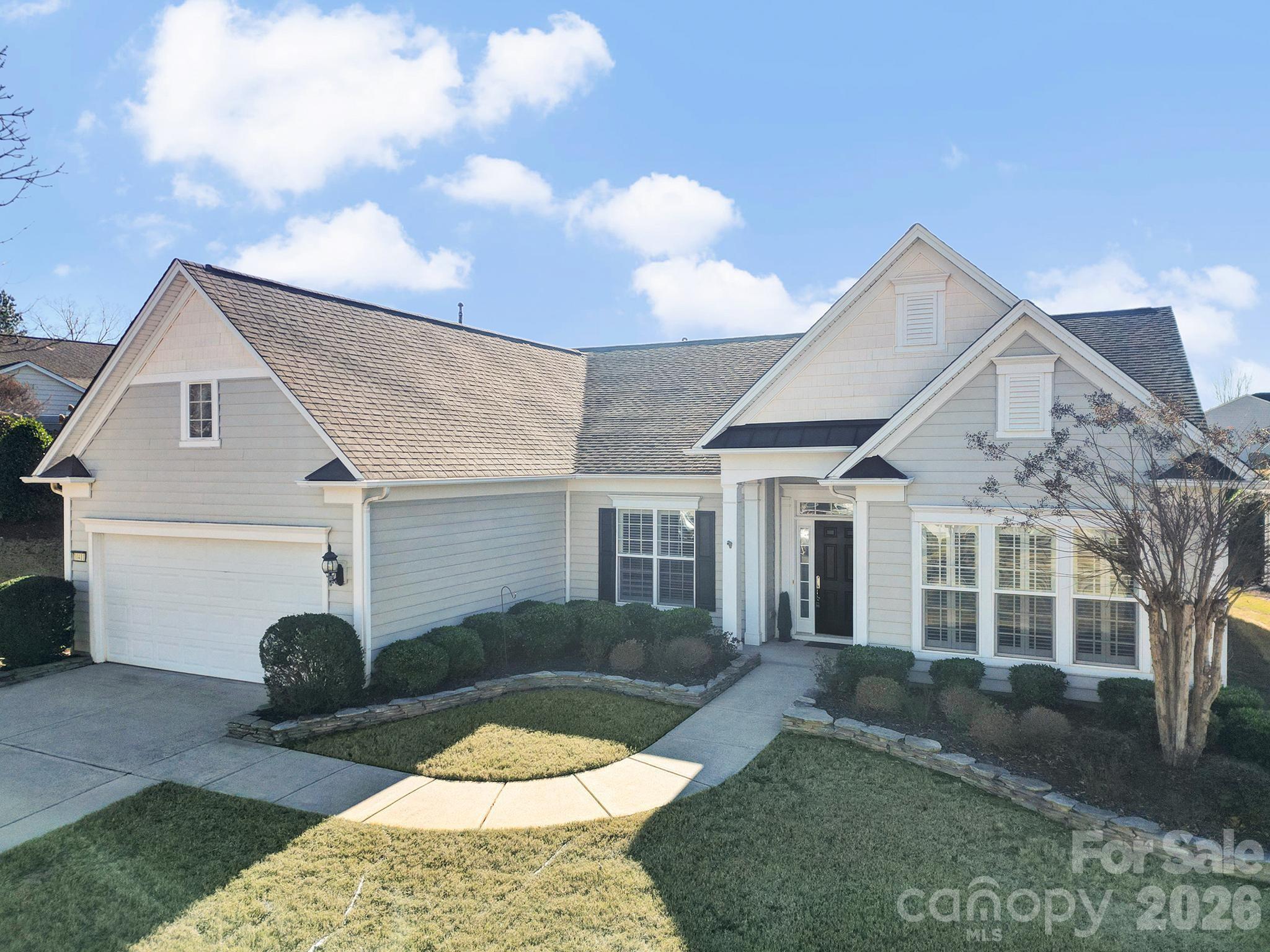 Light-colored house with multiple gables, an attached garage, and landscaped front lawn.