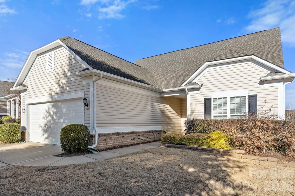 Beige single-story home with an attached garage, gray roof, and landscaped front yard.