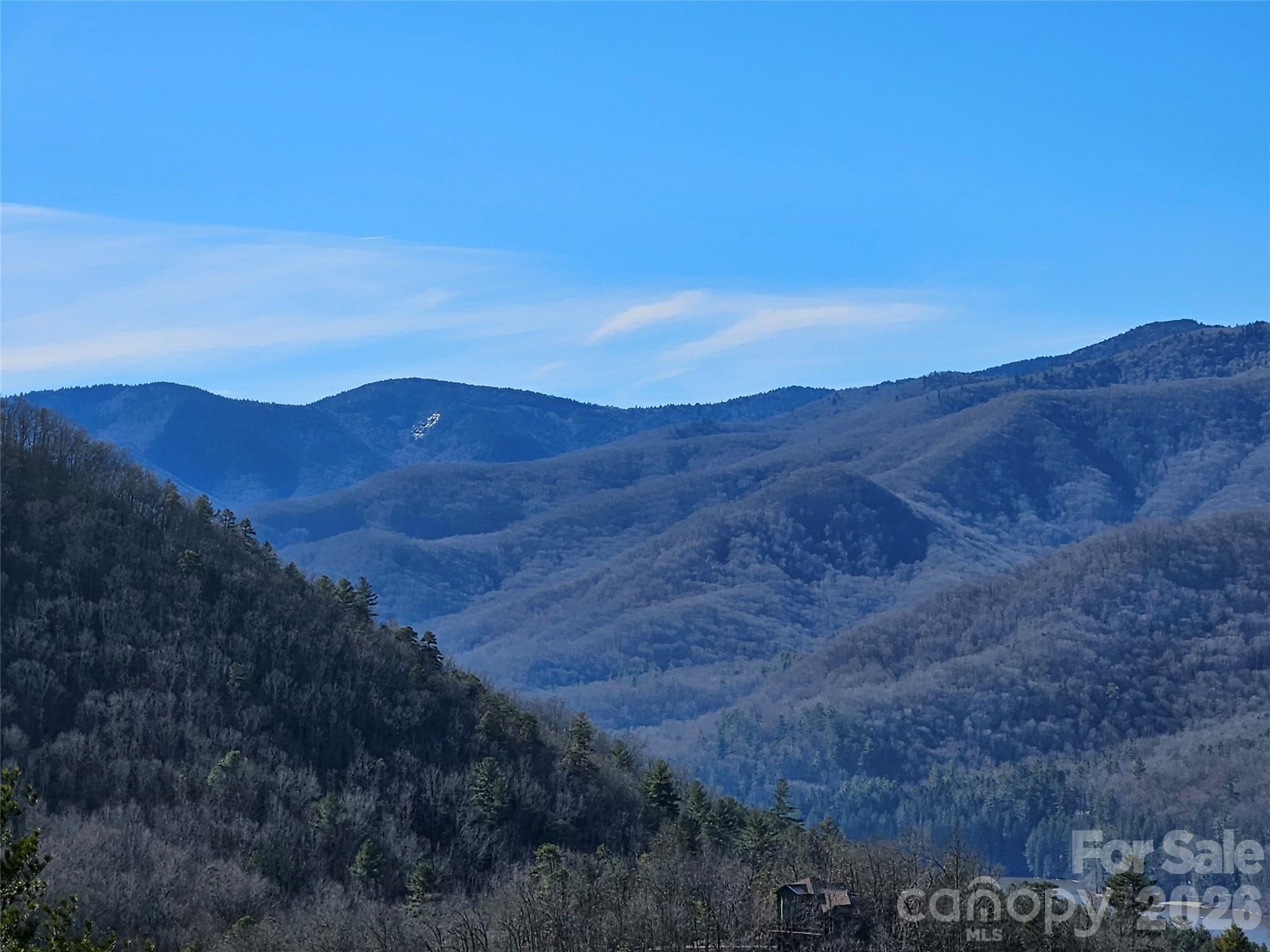 Mountain view with layered forested ridges, blue sky, and a small building in the foreground.