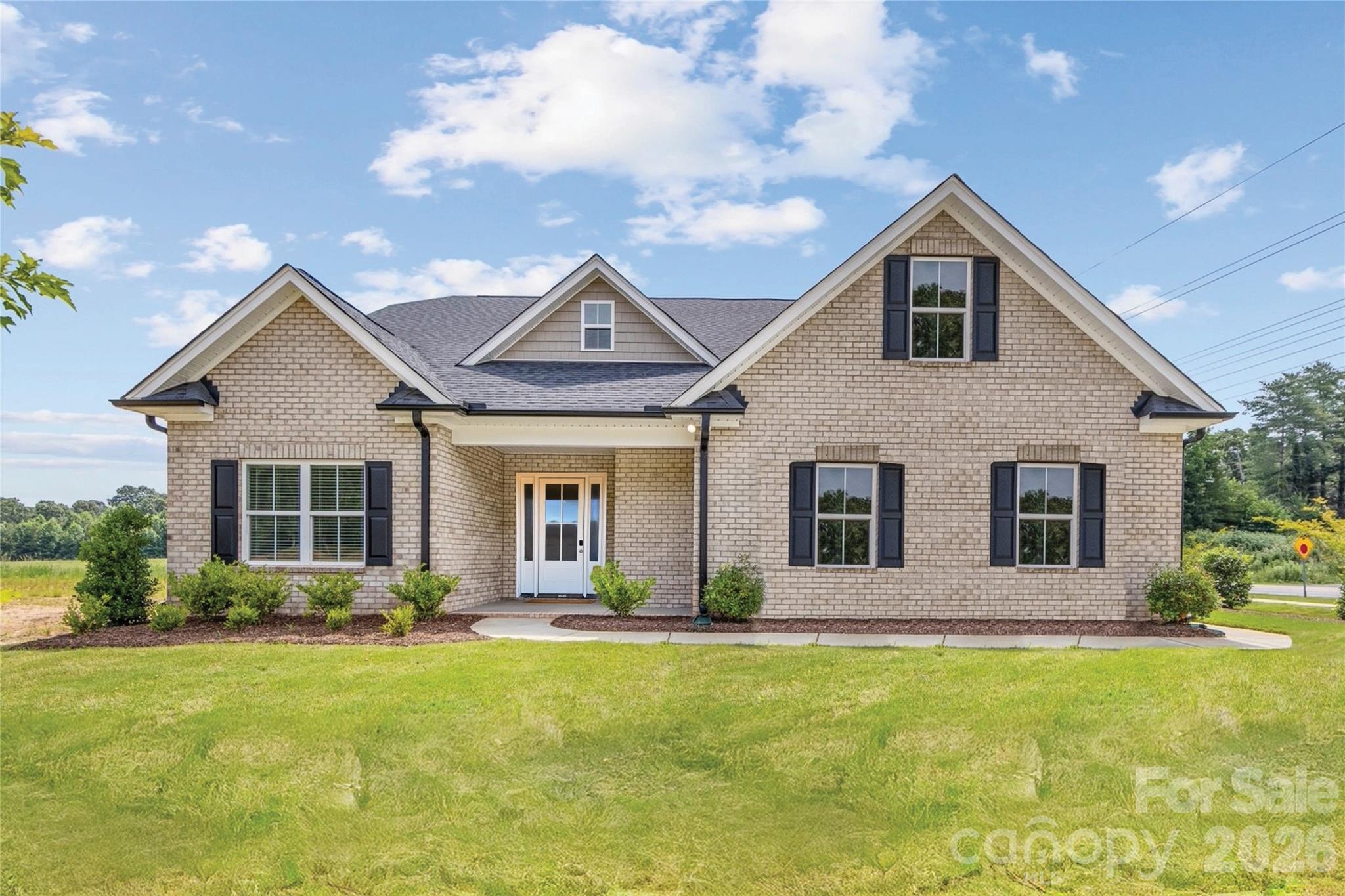 Tan brick house with multiple gables, dark shutters, and a broad front lawn.