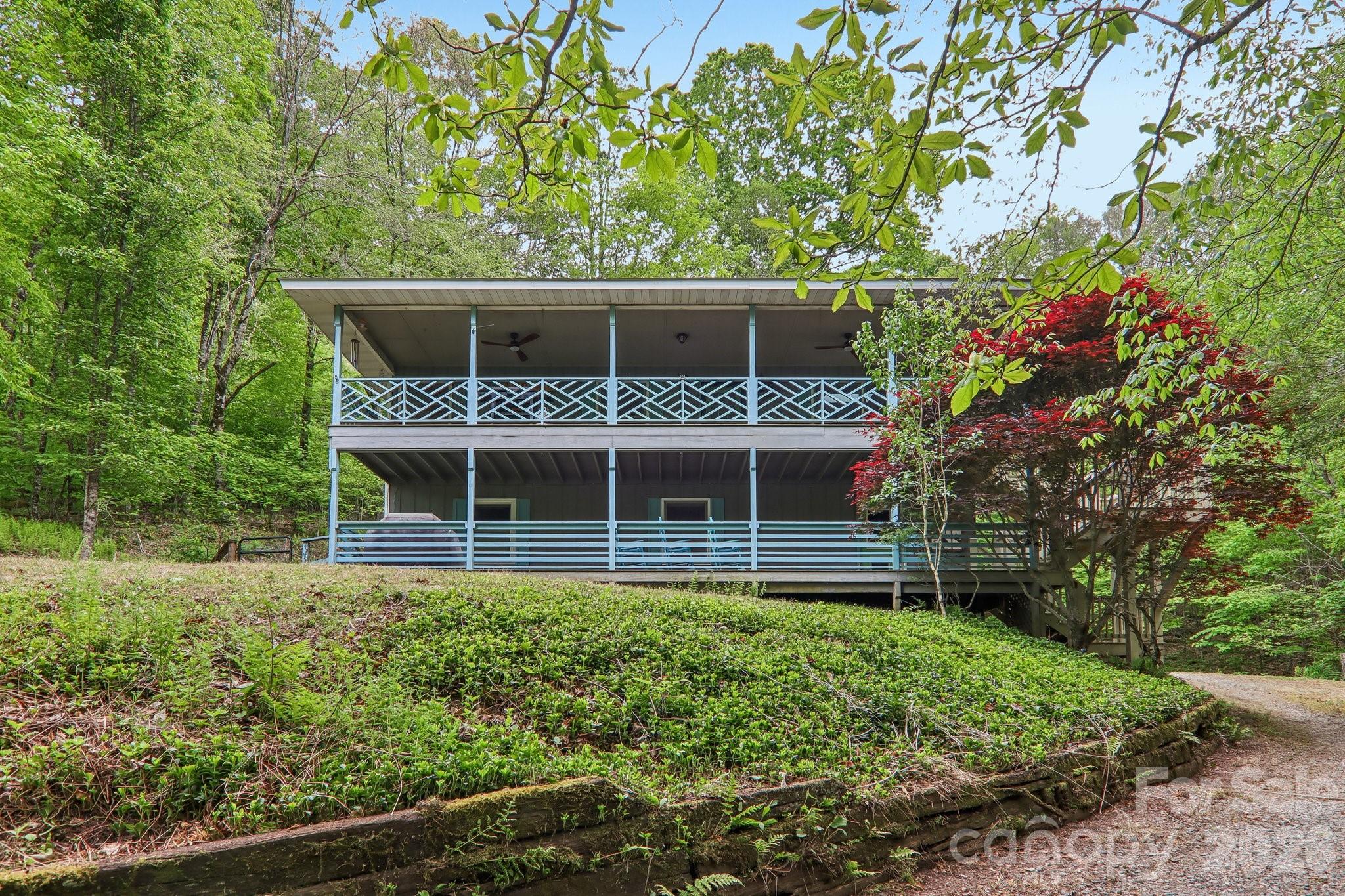 Two-story house with covered porches and pale blue railings on a wooded hillside.