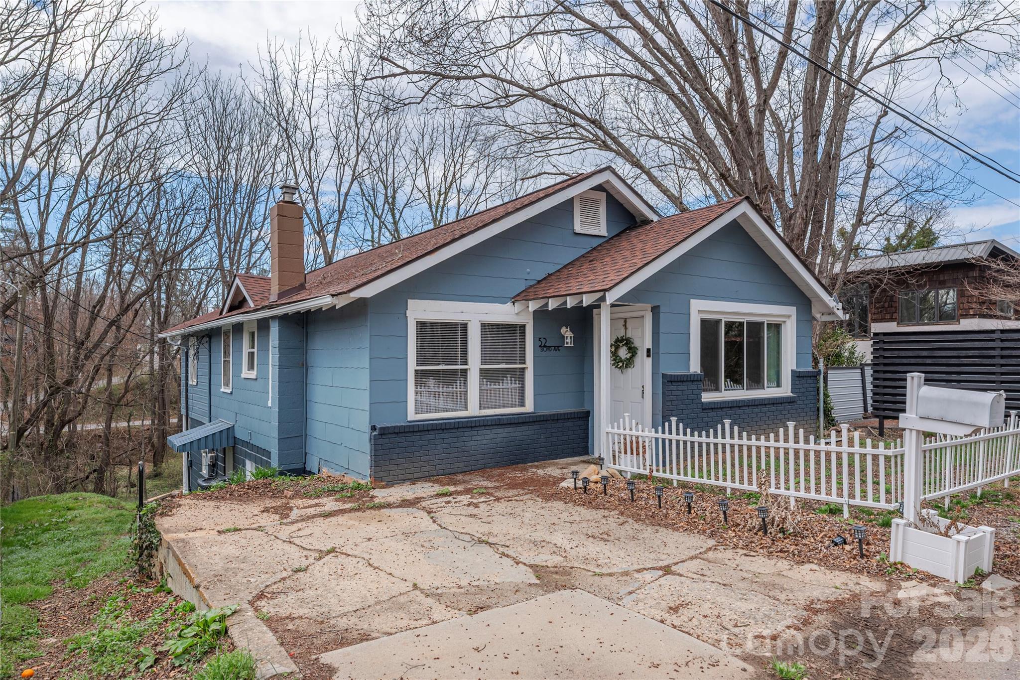 Blue house with white trim, a picket fence, and a wide concrete driveway.