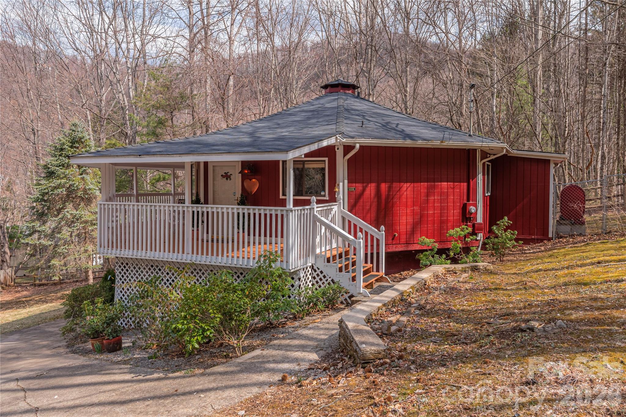 Red single-story home with a covered white-railed porch, surrounded by leafless trees.