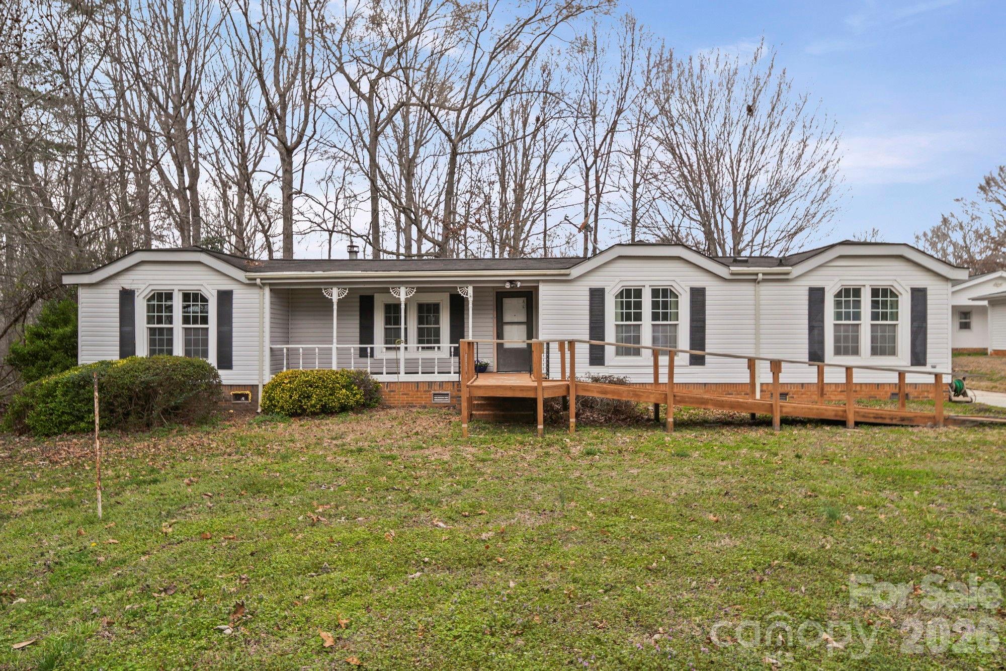 White single-story home with a covered porch and long wooden accessibility ramp.