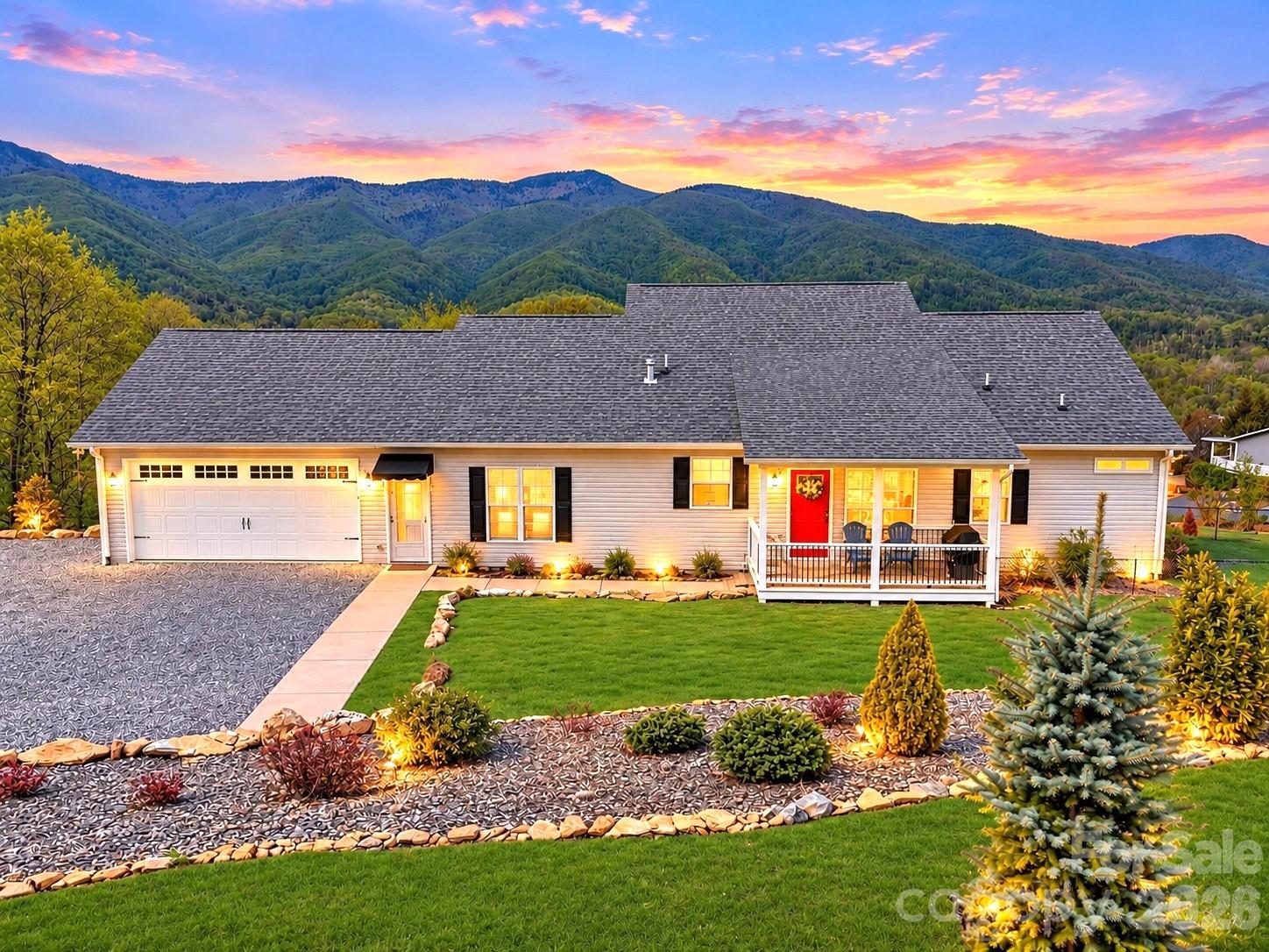 Single-story home with a red front door, landscaped yard, and mountain backdrop at sunset.