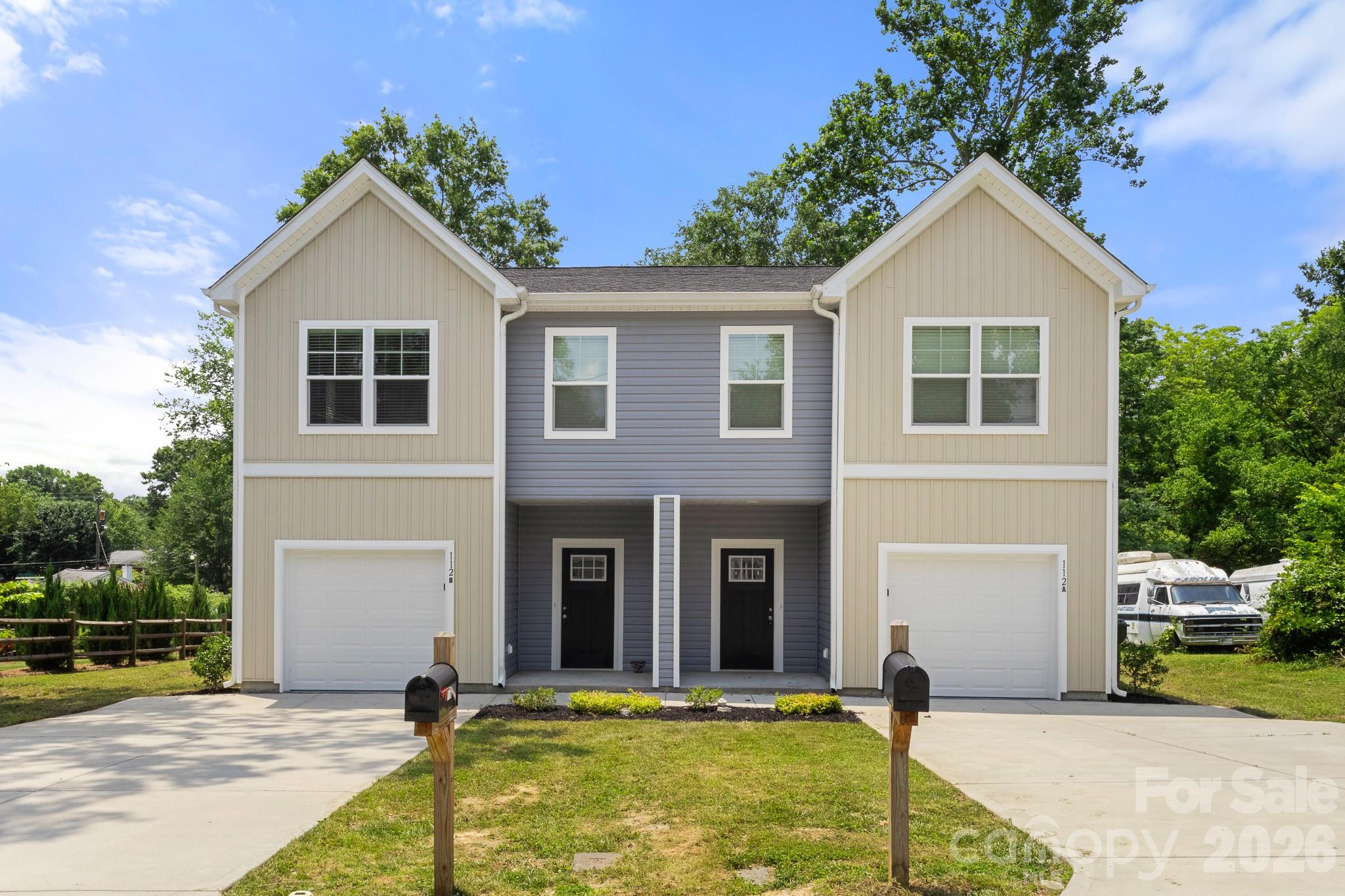 Two-story duplex with cream and gray siding, two garage doors, separate driveways, and front mailboxes.