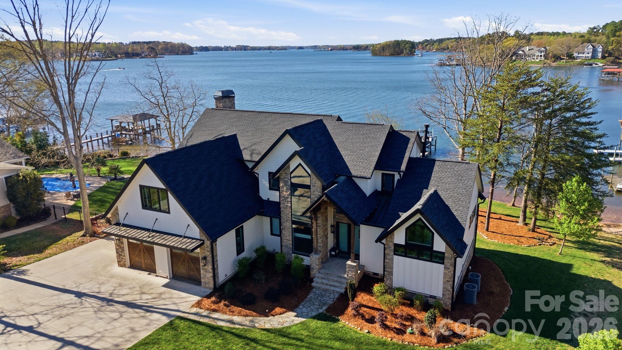Aerial view of a lakeside home with a pool, dock, and broad water views.