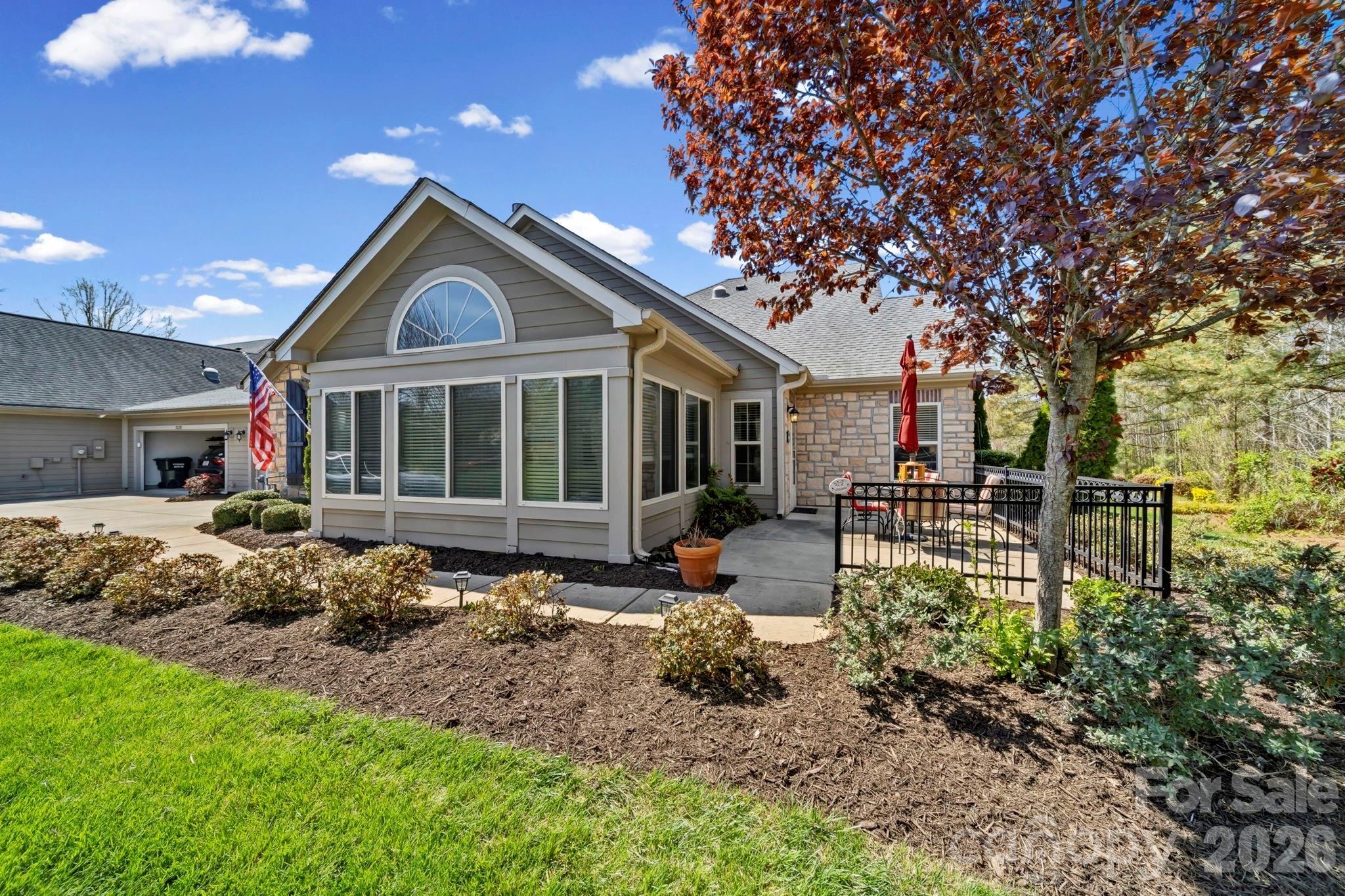 Gray-sided home with stone accents, an attached garage, and a fenced patio beneath a red-leaved tree.