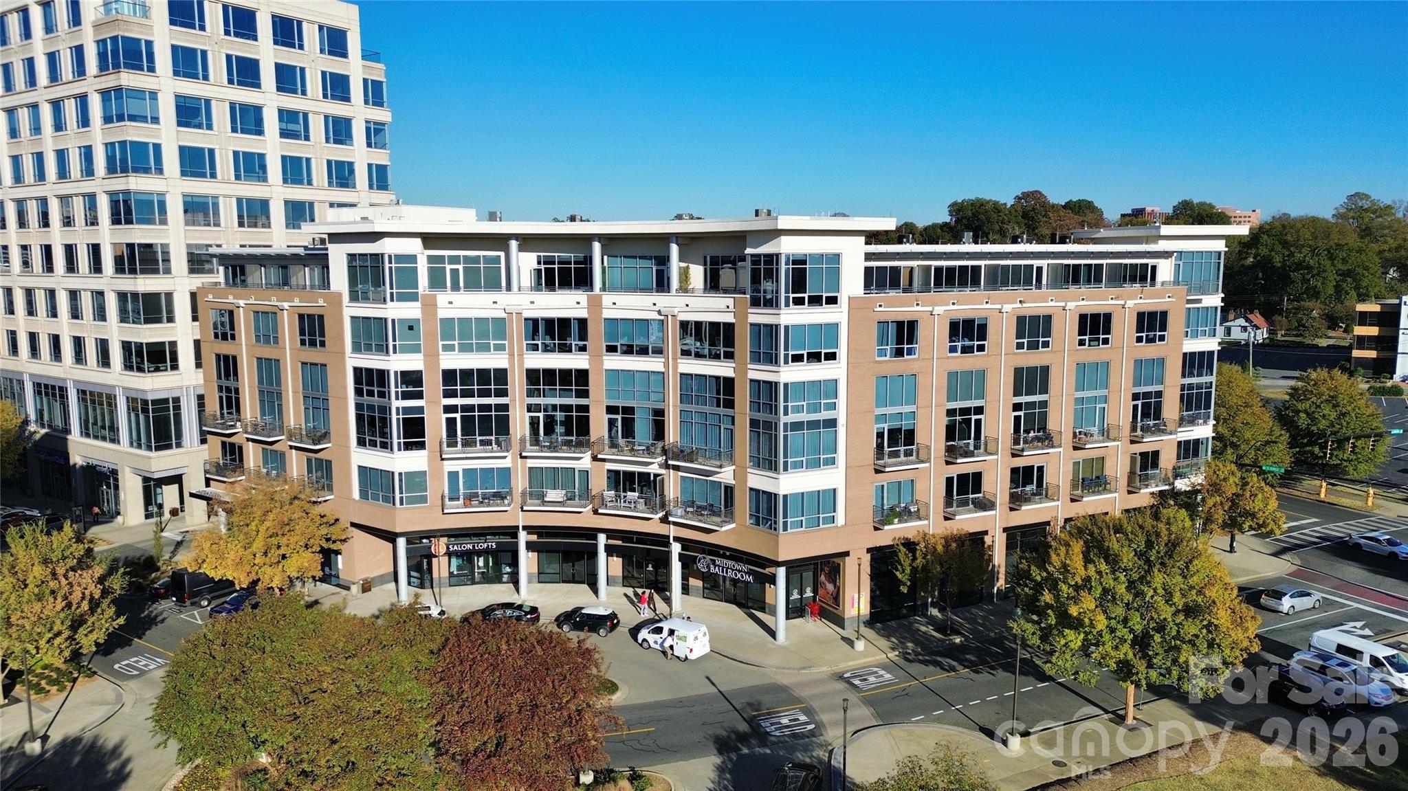 Modern condominium building with balconies and ground-floor businesses, viewed from above on a sunny autumn day.