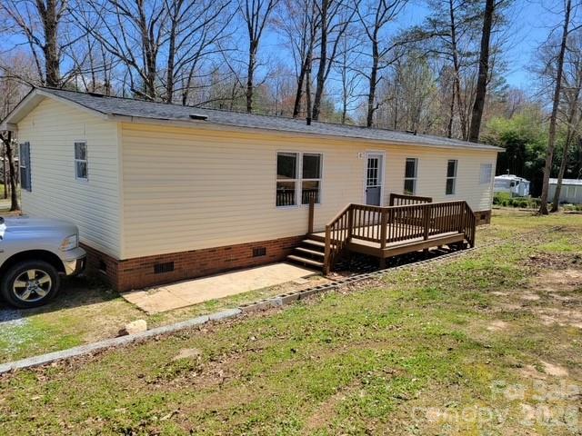 Manufactured home with a raised wooden deck and brick foundation, among leafless trees.