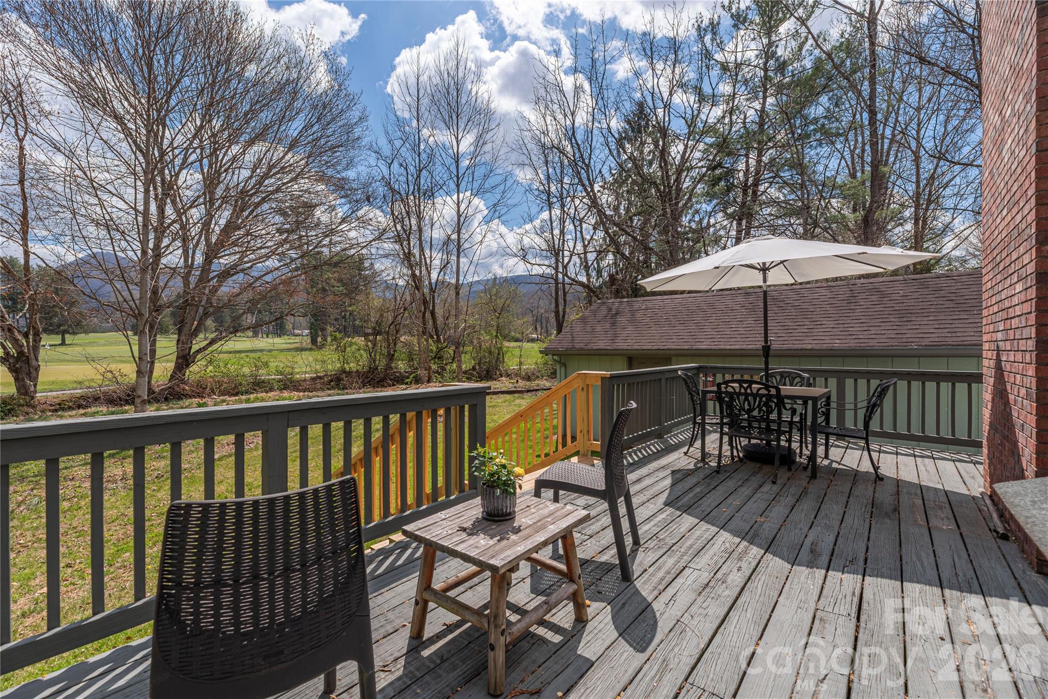 Furnished deck with a white umbrella overlooks a golf course and distant mountains.