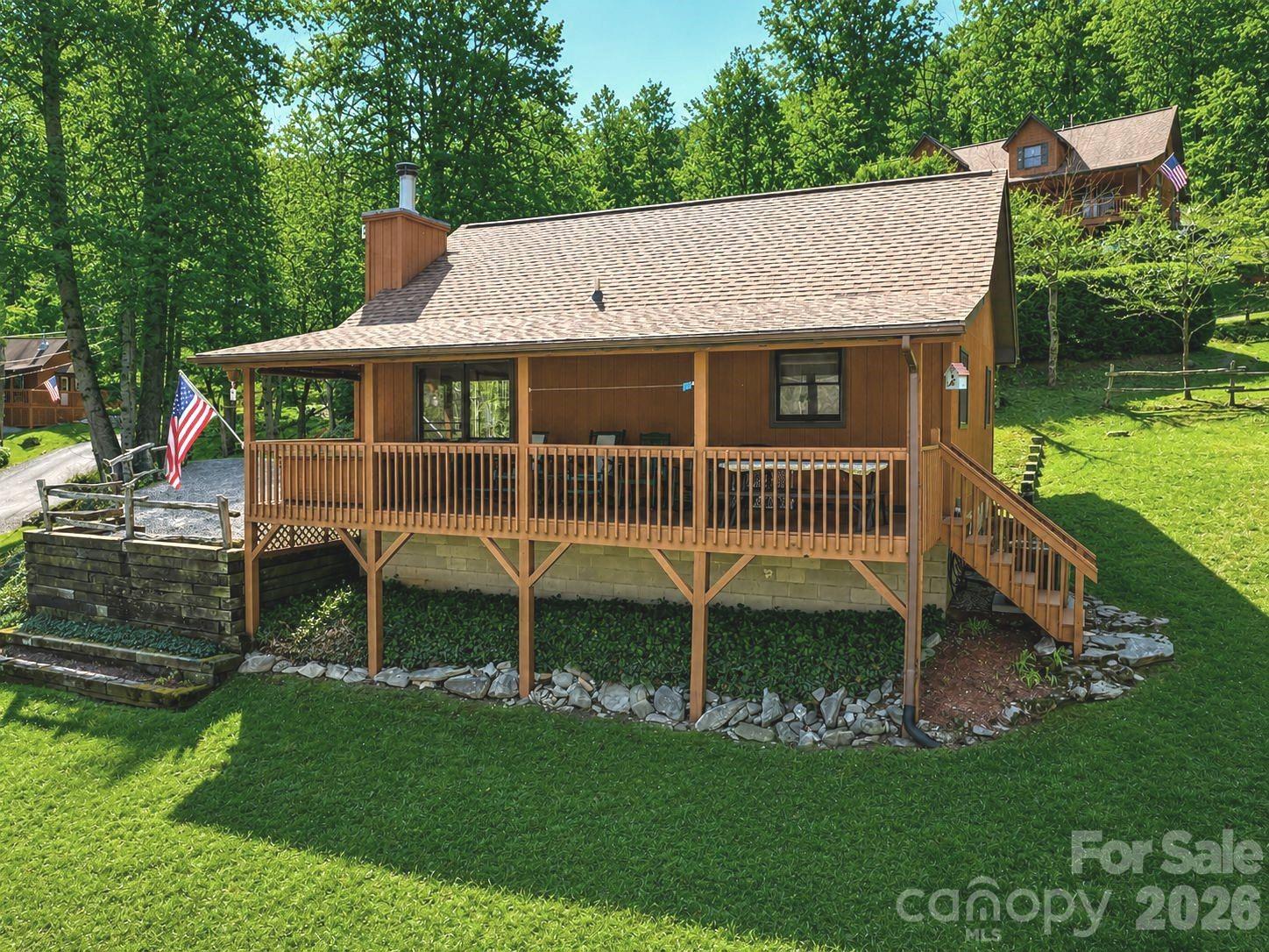 Wood cabin with a broad raised porch and stairs, surrounded by lawn and trees.
