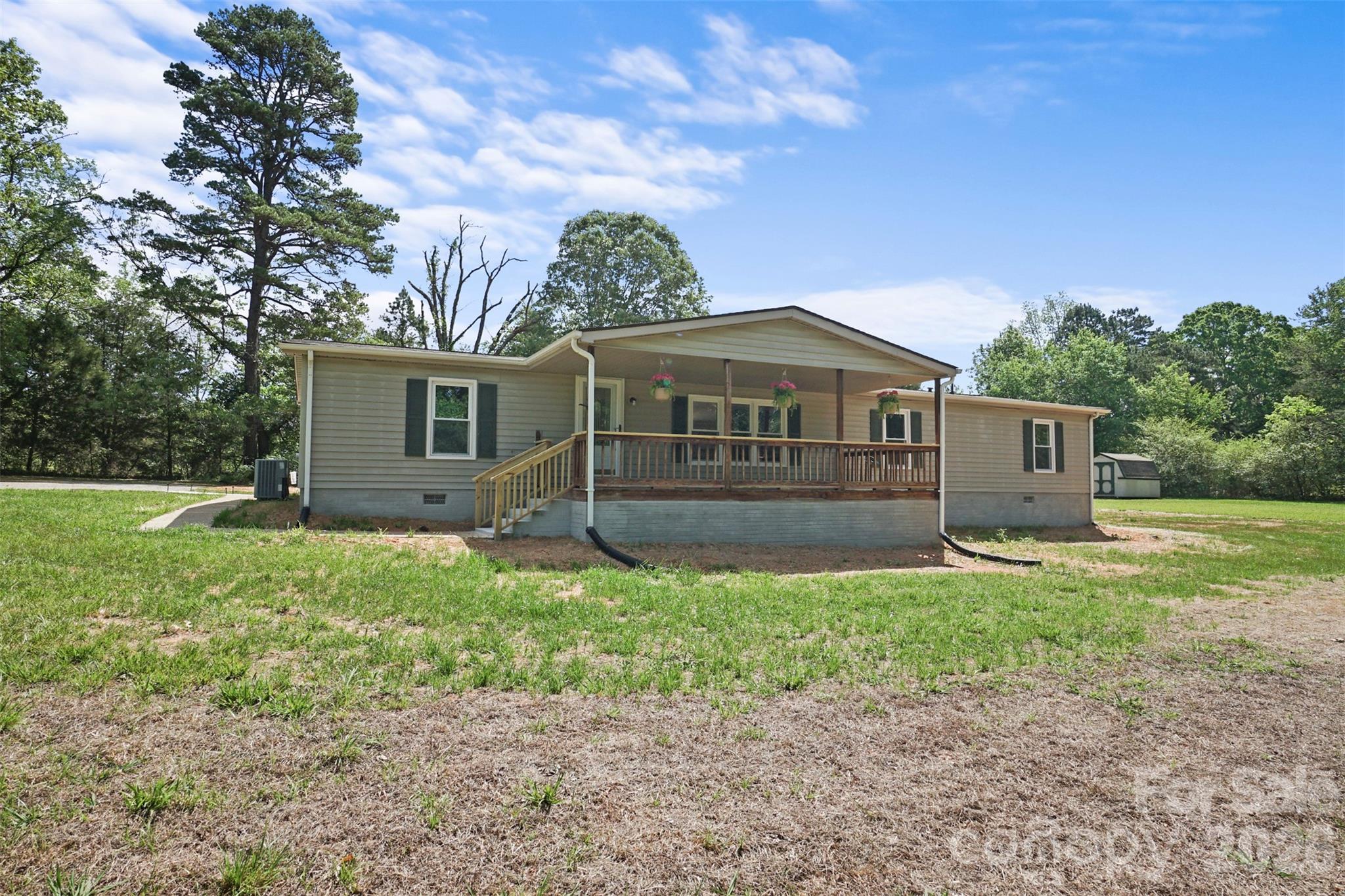 Single-story beige home with a broad covered porch, wooden railings, and hanging flower baskets.