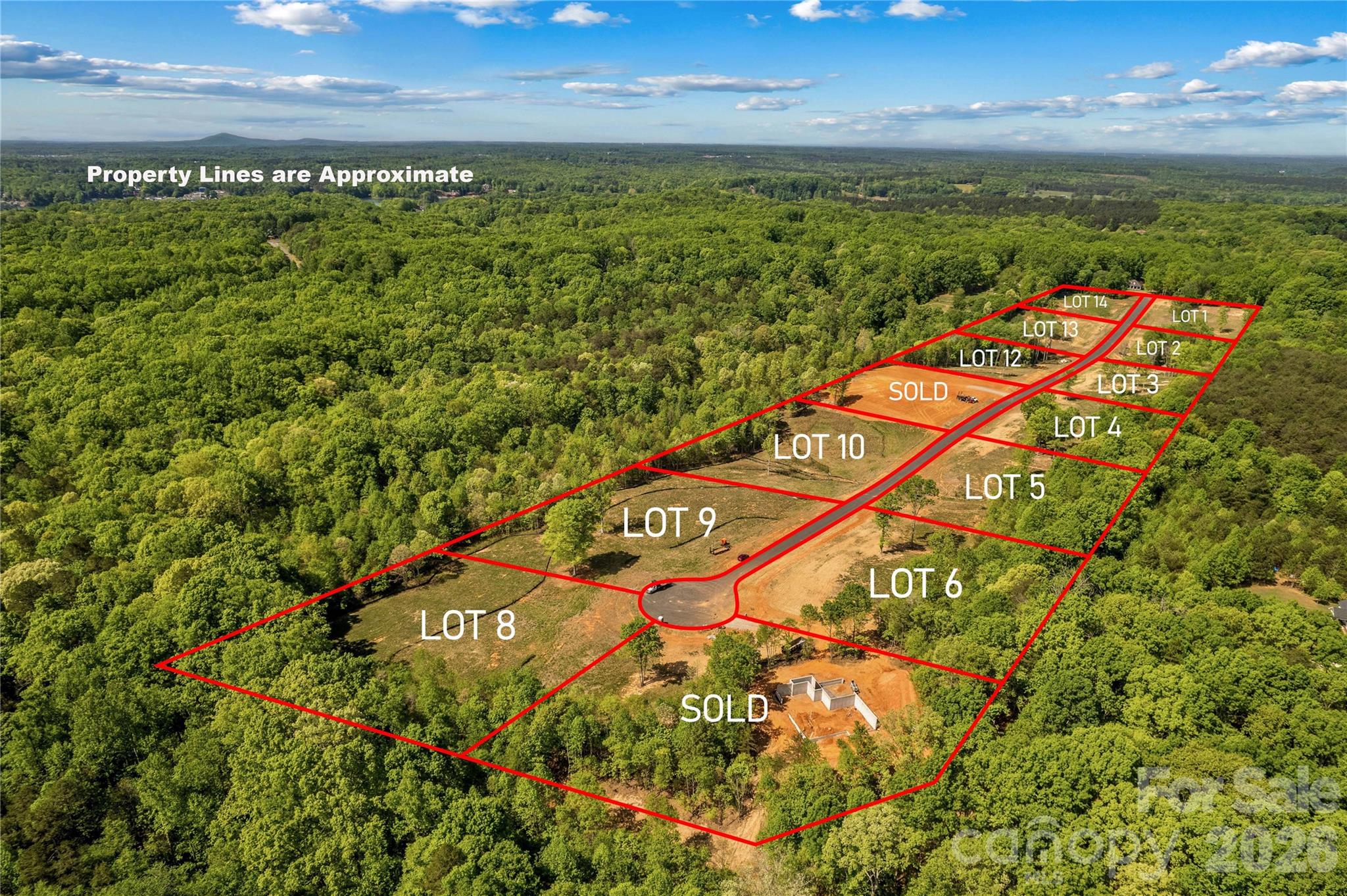 Aerial subdivision of wooded land with red lot boundaries, labeled parcels, a central road, and two lots marked sold.