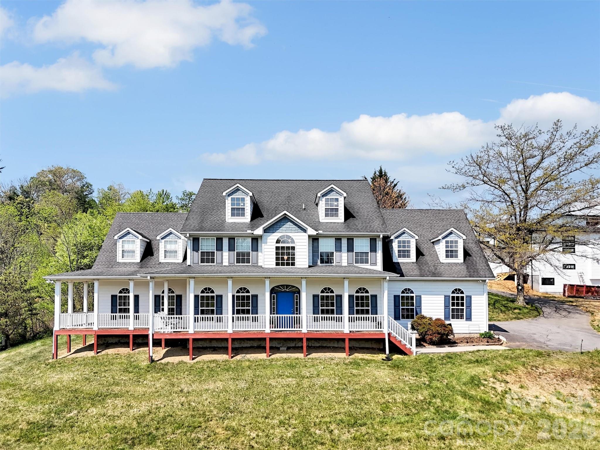 White multi-dormer home with a long covered porch and bright blue front door