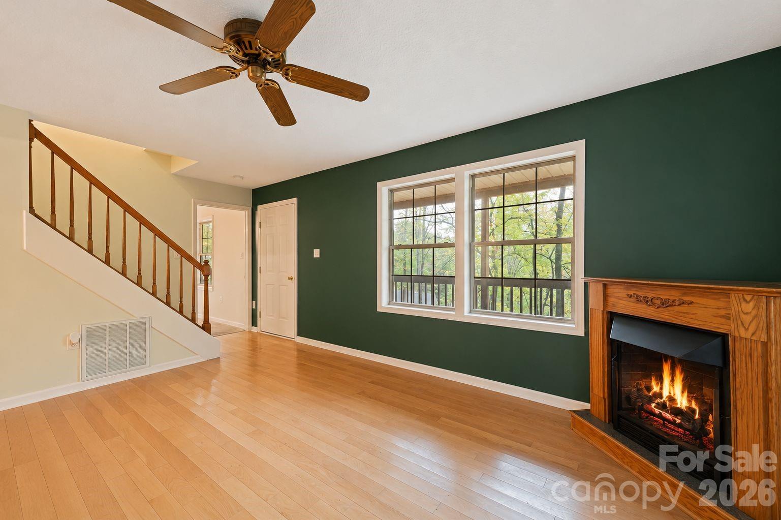 Living room with a green accent wall, wooden fireplace, staircase, and light wood floors.