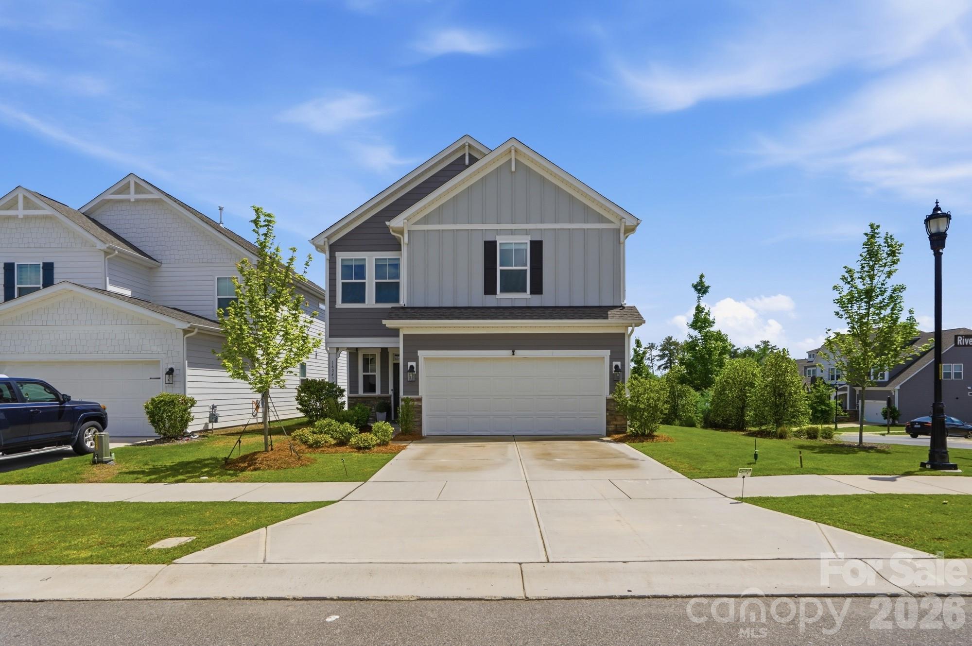 Two-story gray house with a double garage, broad driveway, and young trees.
