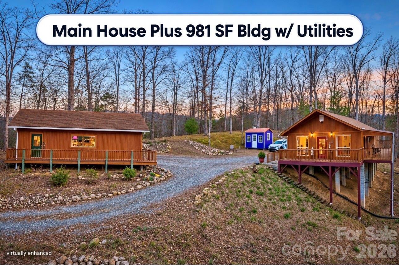 Two wood-sided buildings and a small blue outbuilding sit along a wooded gravel drive.