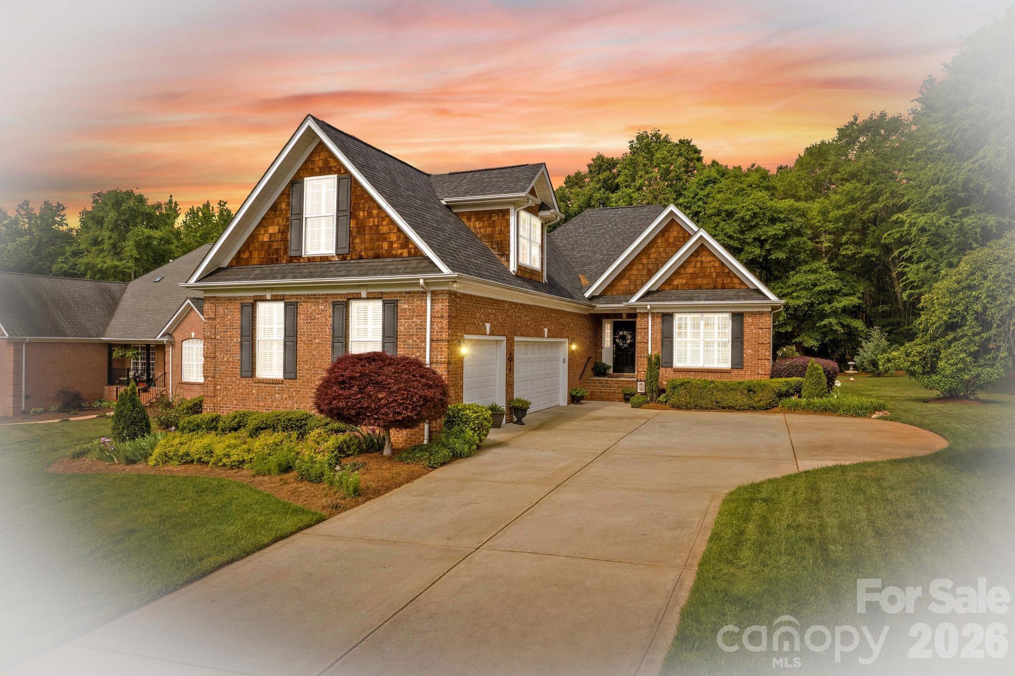 Two-story brick house with peaked gables, cedar-shingle accents, landscaped yard, and a curved driveway.