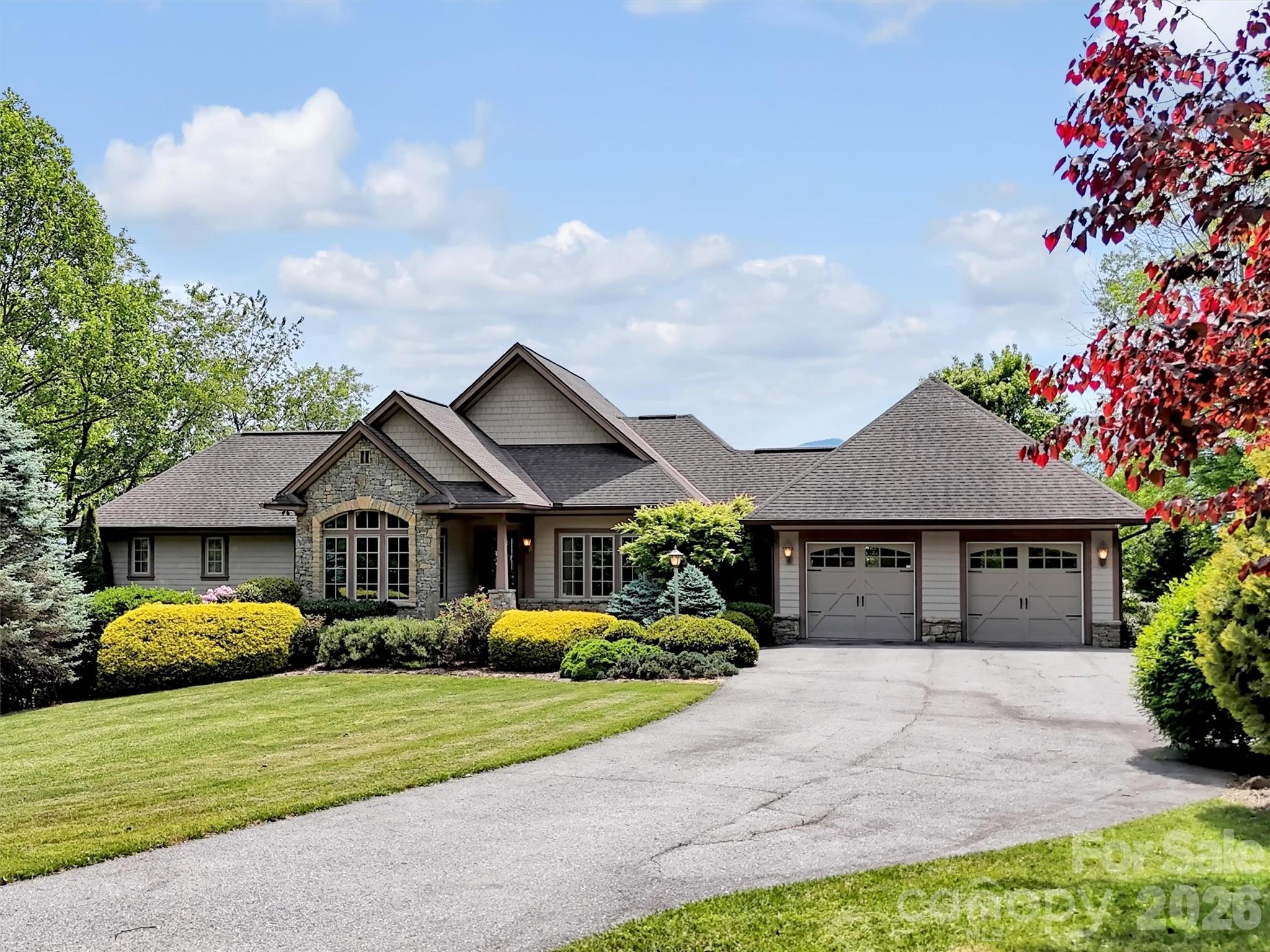 Large gray-and-stone home with a two-car garage, landscaped lawn, and red autumn leaves.